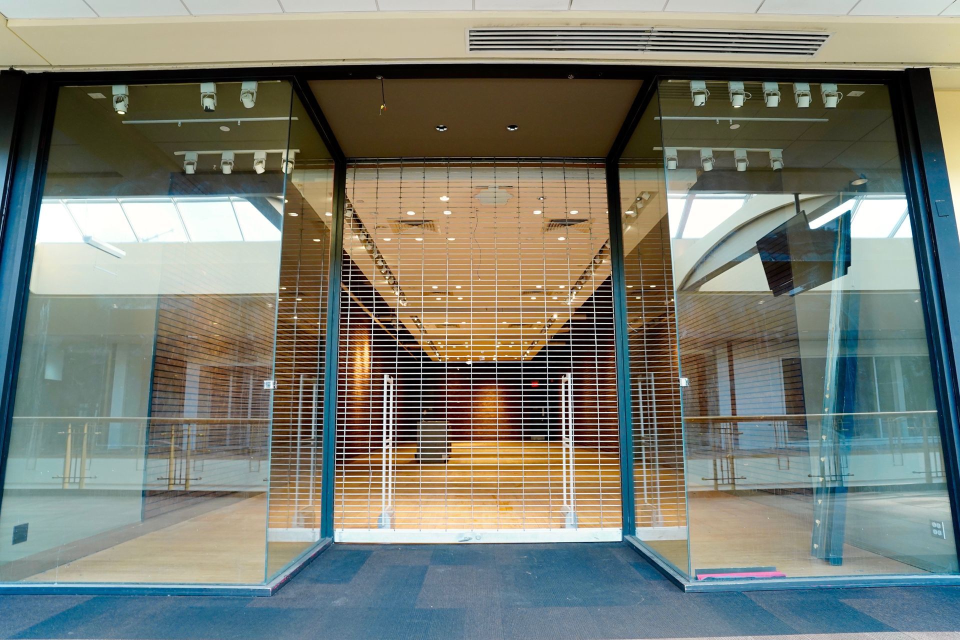 A storefront with a closed metal security gate behind glass doors in a brightly lit indoor mall hallway.