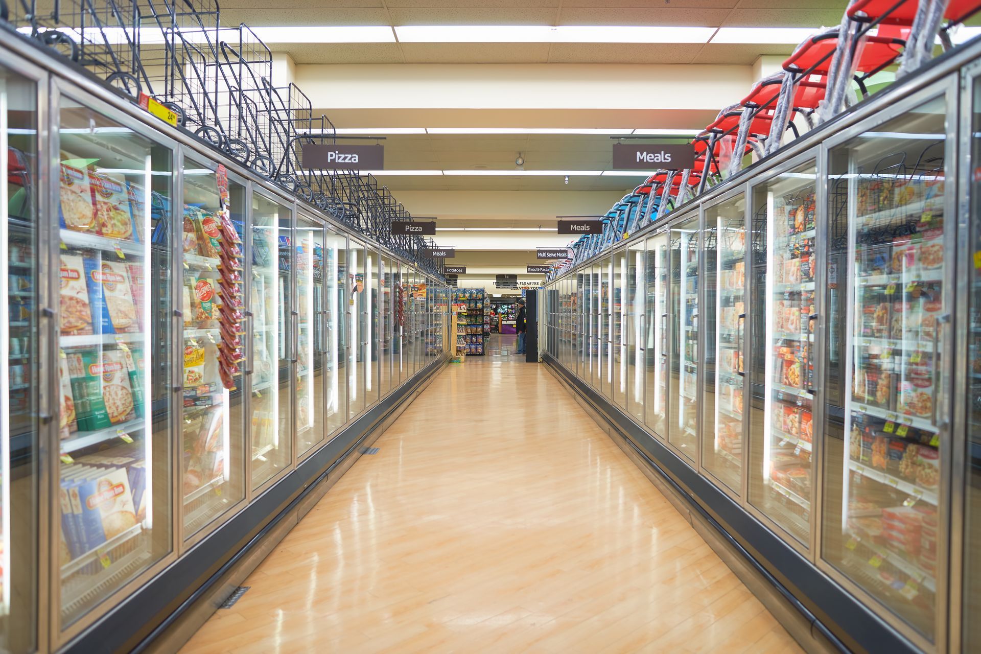 A supermarket aisle lined with long rows of glass-door refrigerated freezer cabinets on both sides.