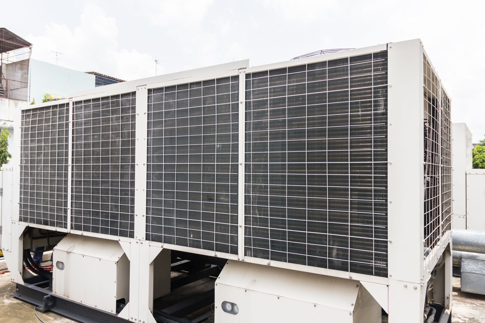 A row of metallic industrial exhaust fans with curved ductwork pipes stands on a flat, cloudy commercial rooftop.