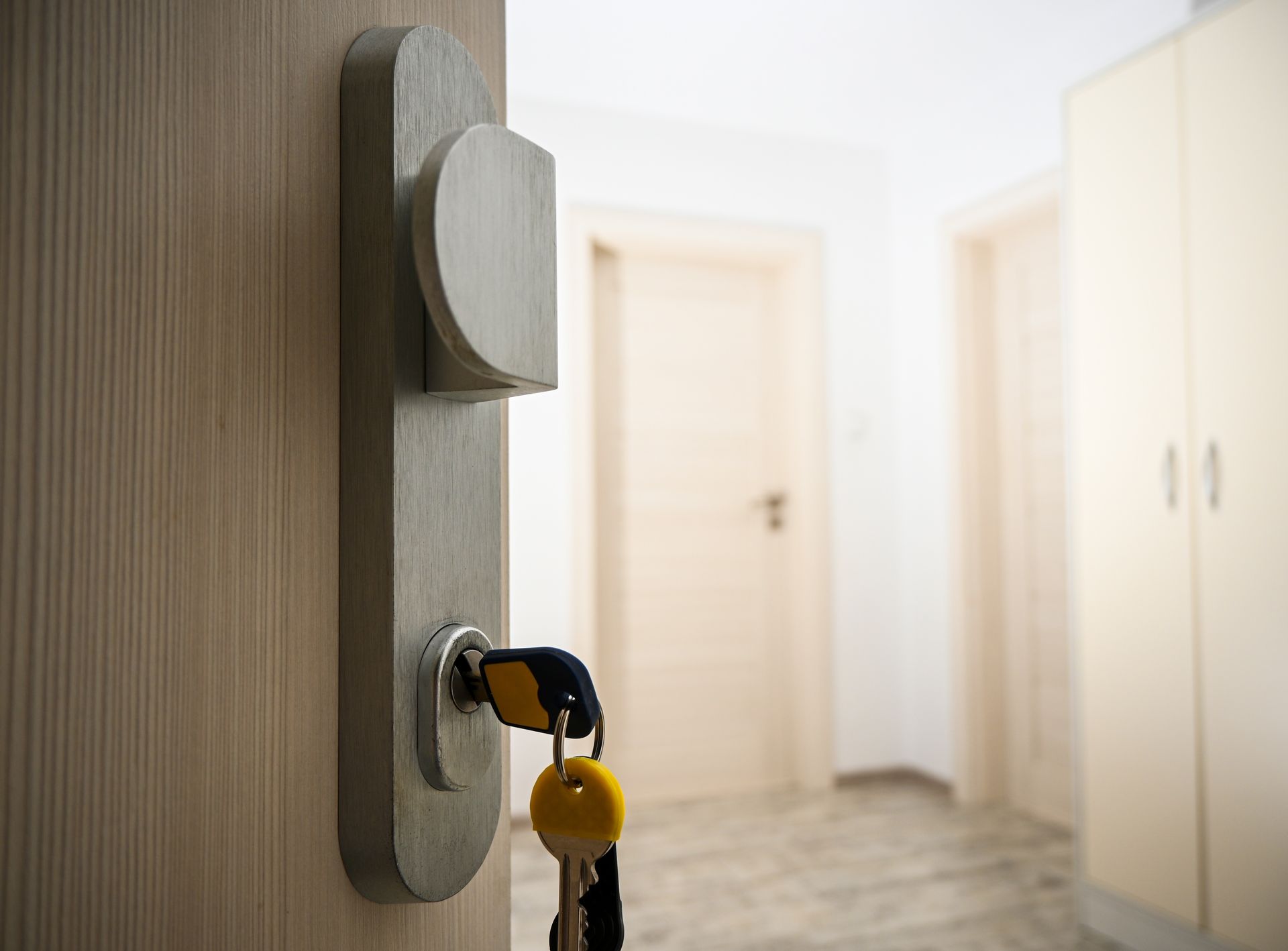 A close-up of a light-colored wooden door handle with yellow keys inserted into the lock, in a bright home hallway.
