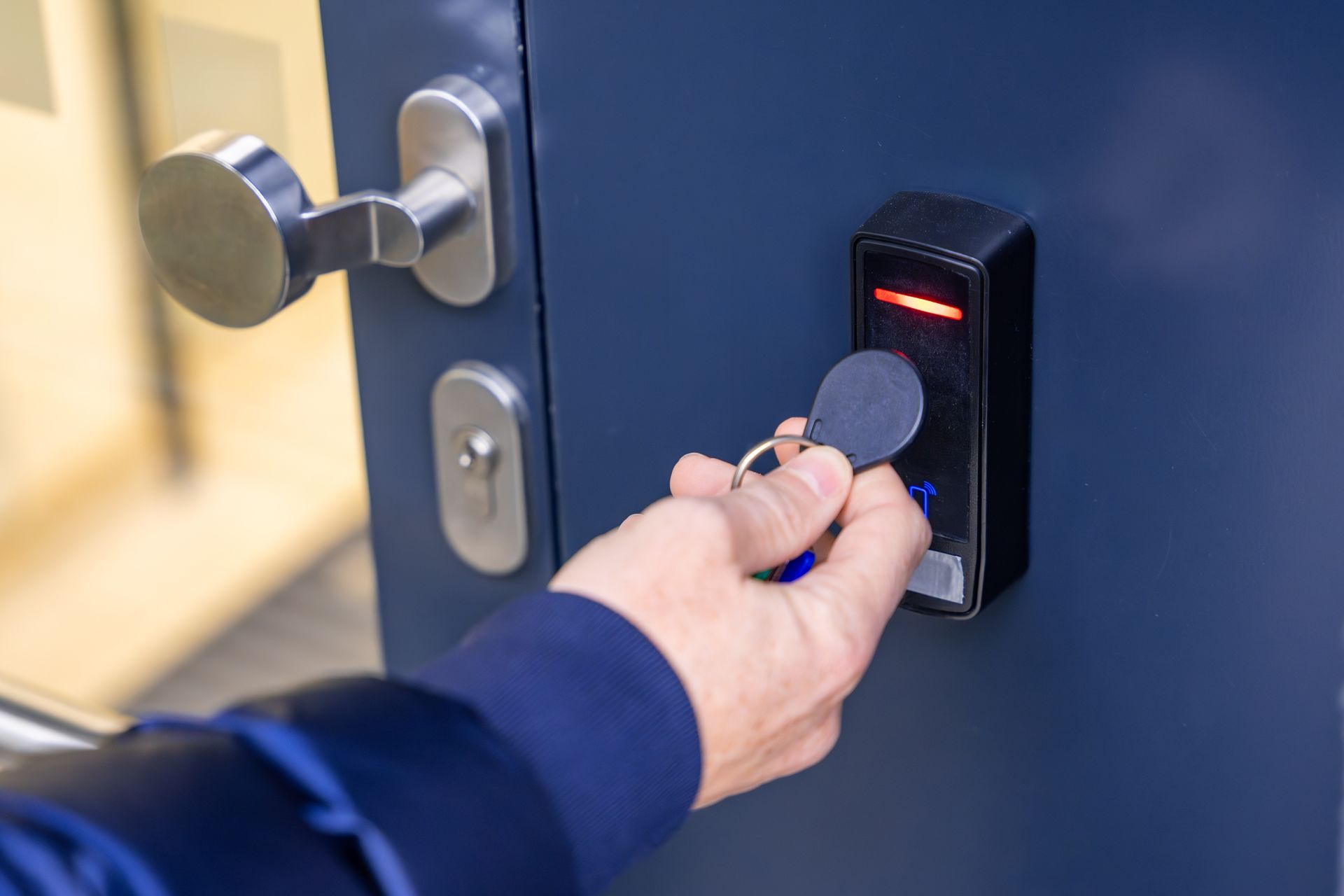 A hand holds a key fob against an electronic access control reader on a blue door.