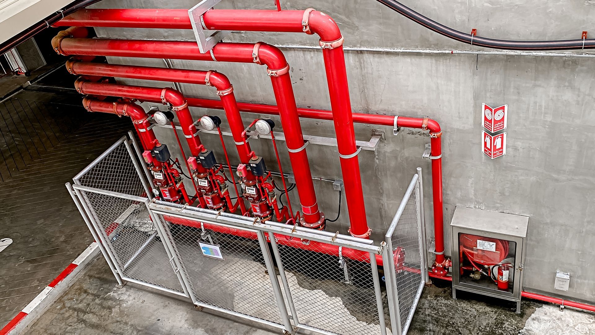 A row of bright red vertical fire sprinkler pipes enclosed in a metal security cage against a grey concrete wall.