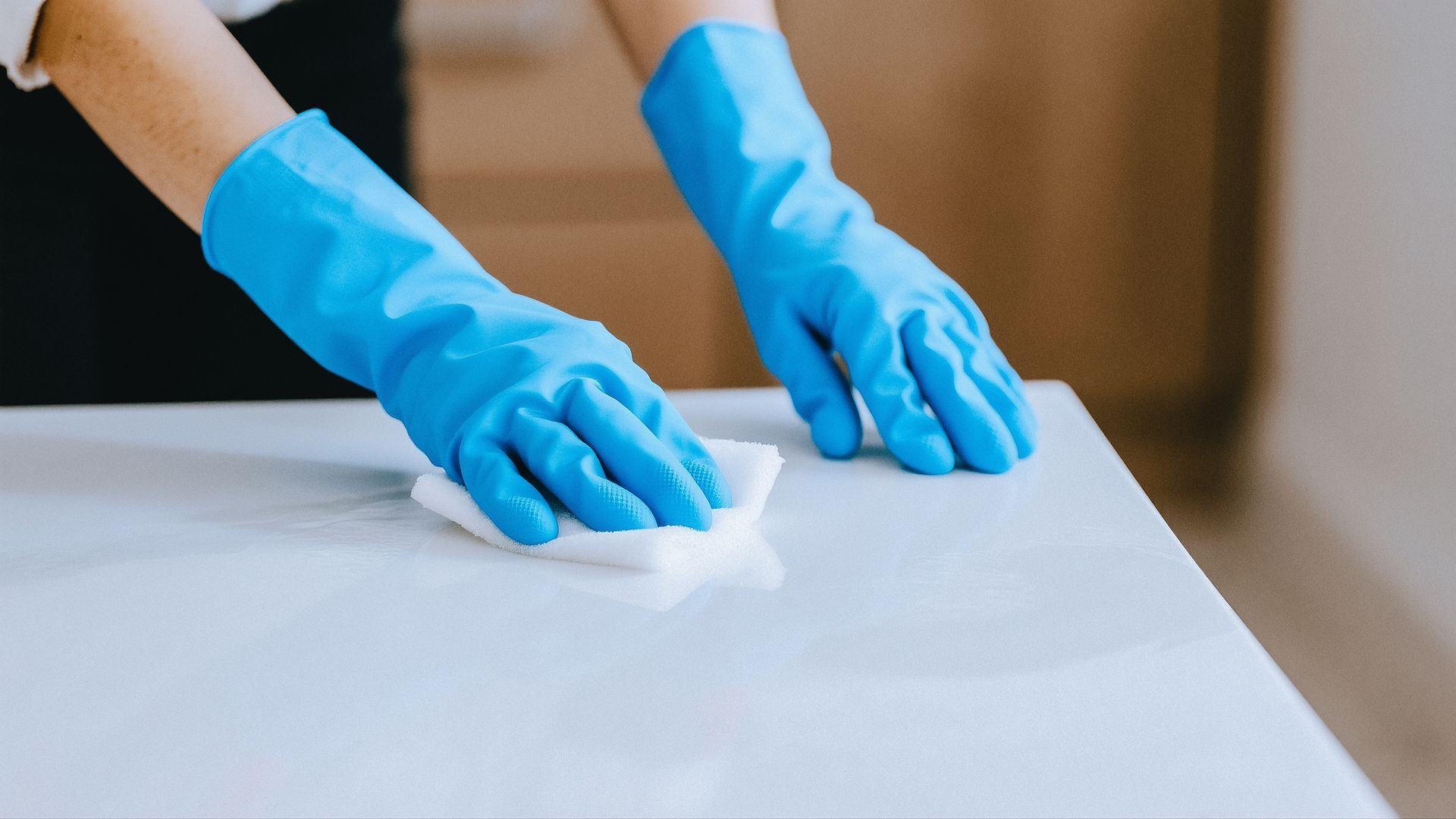 A person wearing blue rubber gloves wipes a white surface with a white cloth.