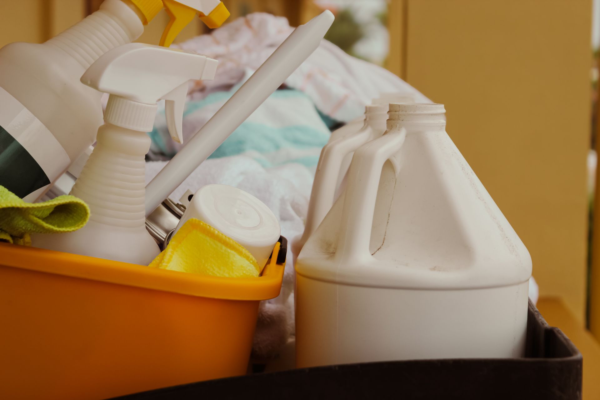 An orange caddy filled with various white plastic cleaning spray bottles and a container, next to white jugs.