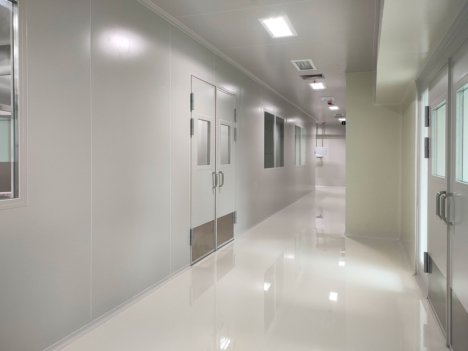 A clean, sterile hallway with white walls and reflective flooring, featuring multiple doorways and recessed lighting.