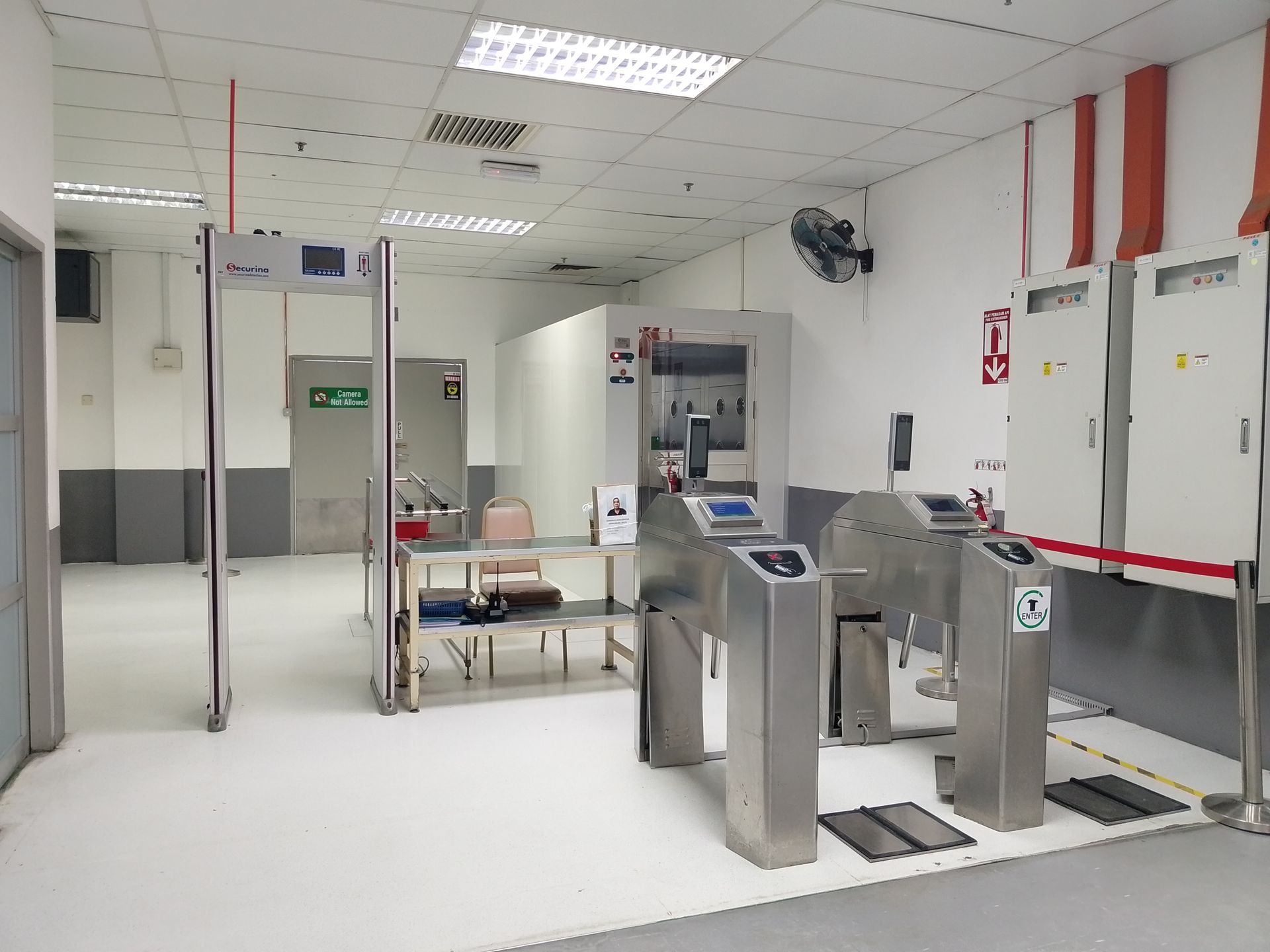 A security checkpoint with a walk-through metal detector, a small table, and two stainless steel turnstiles in an office.