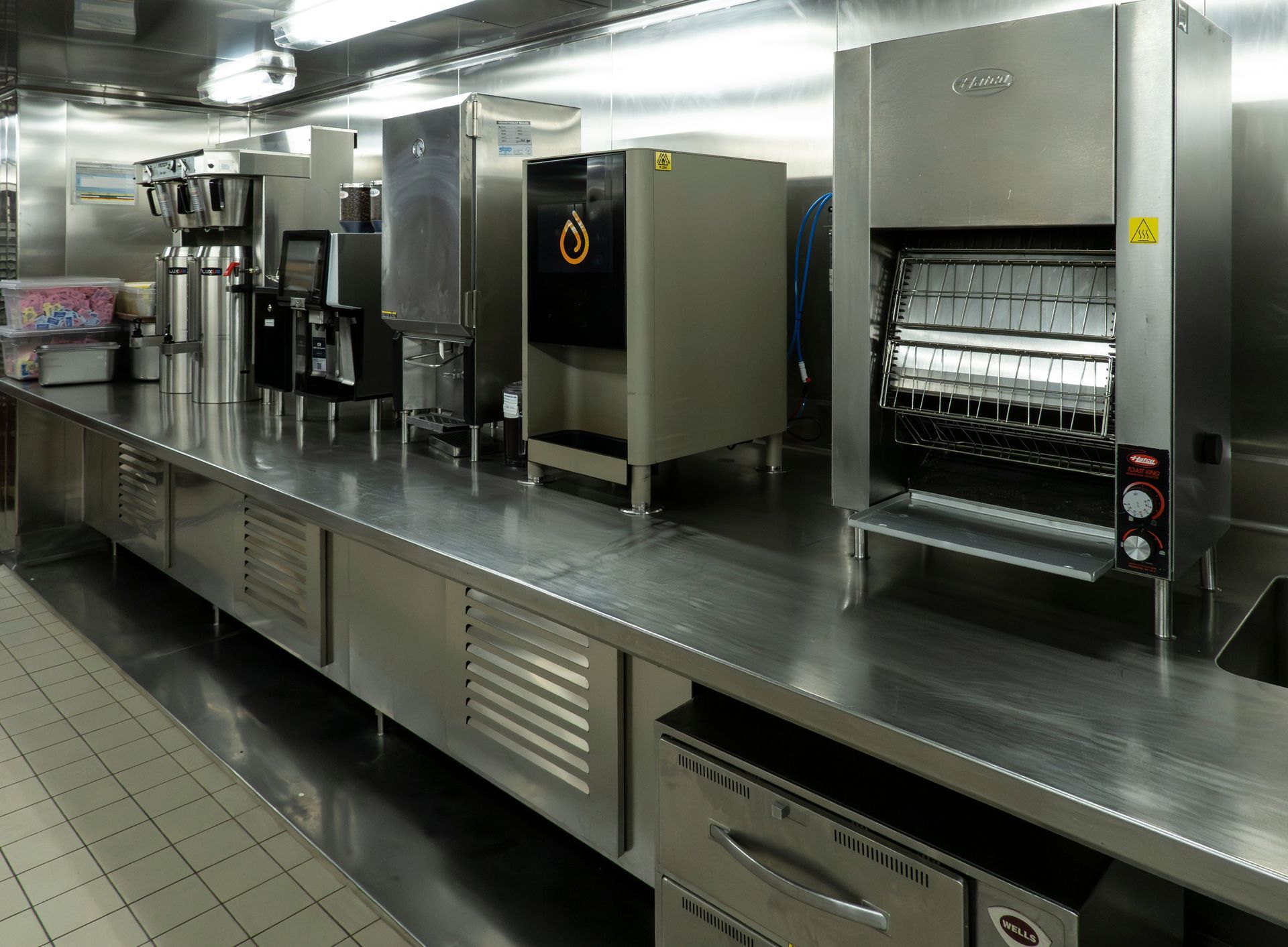 Commercial kitchen featuring a long stainless steel countertop with several pieces of industrial food equipment.
