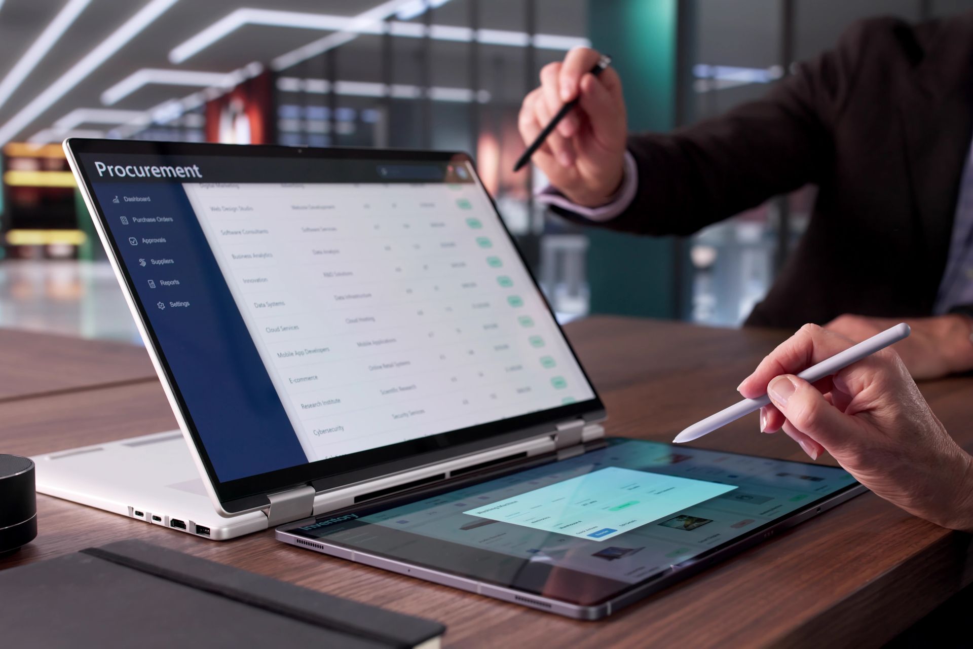 Two people use styluses on a convertible laptop with a dual-screen display in a professional office setting.
