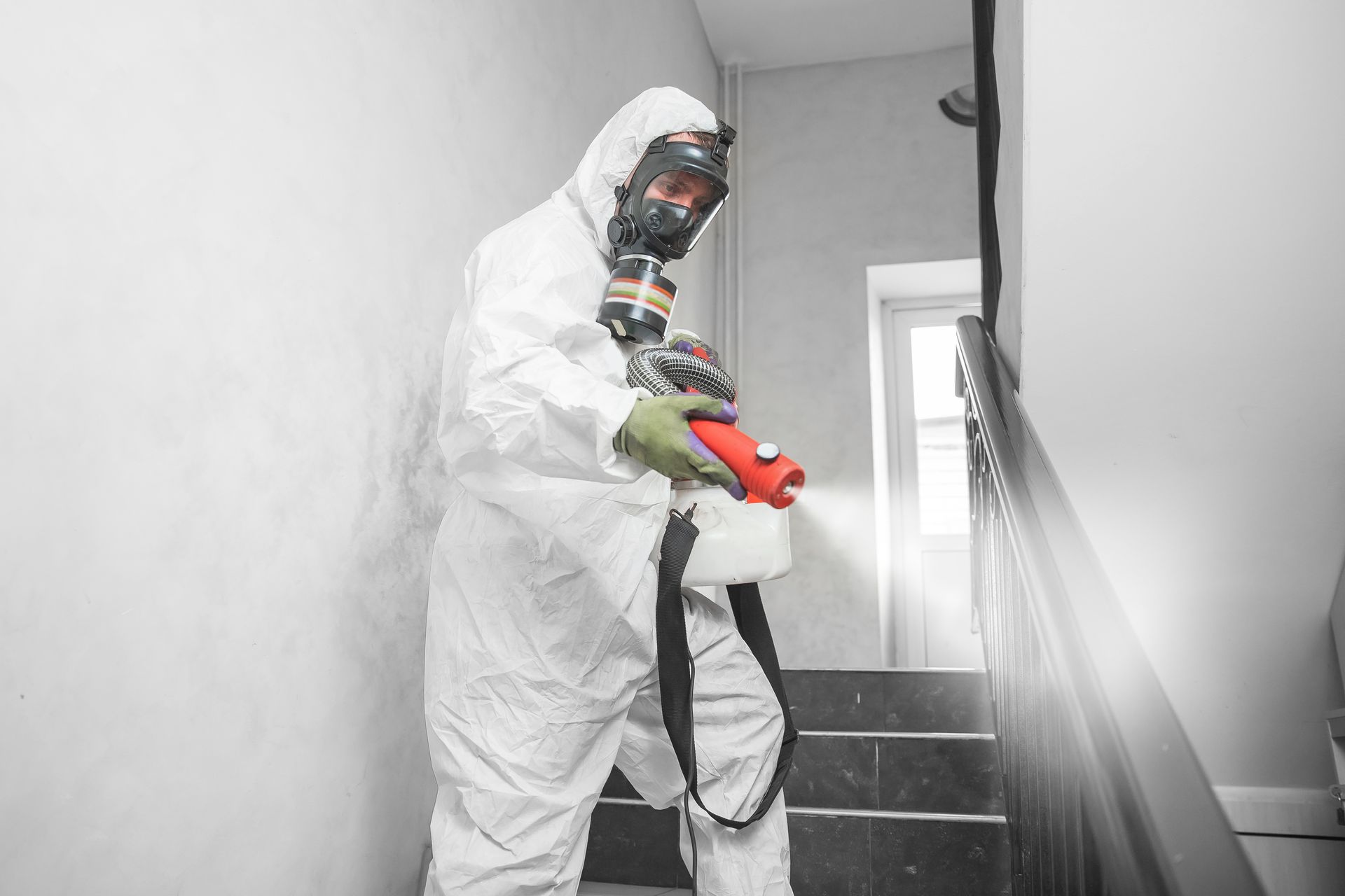 A person in a white hazmat suit and respirator sprays disinfectant on a staircase.