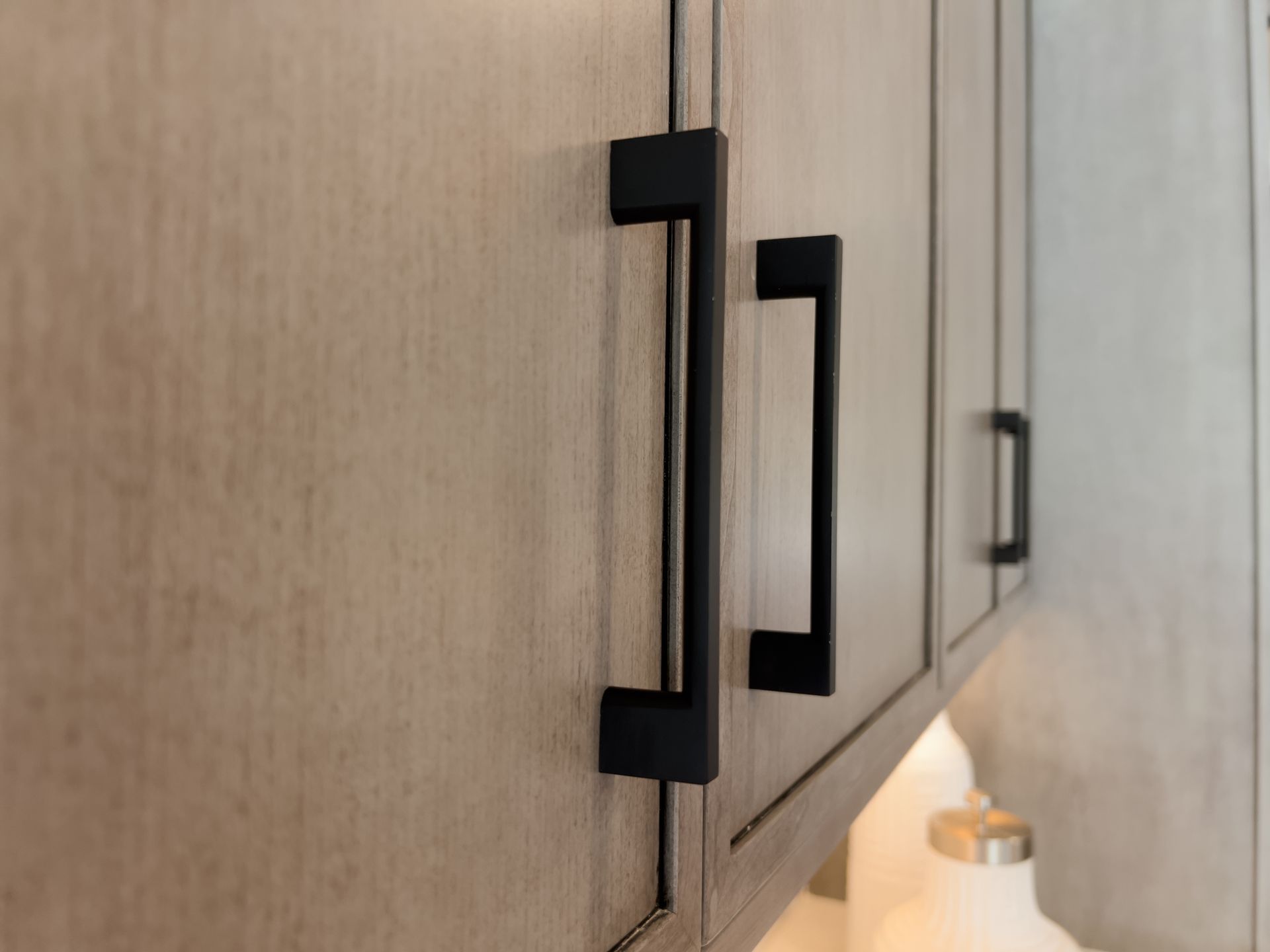 A close-up of matte black rectangular cabinet pulls on light-toned, wood-grained kitchen cabinets.