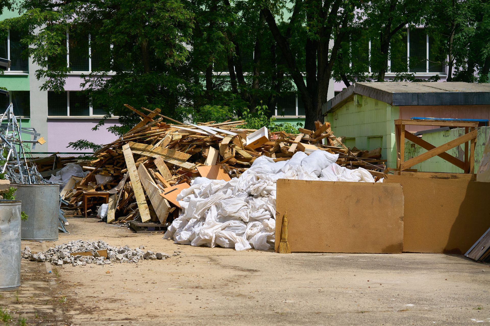 A large pile of construction debris and white bags of rubble sitting on a gravel lot near a building.