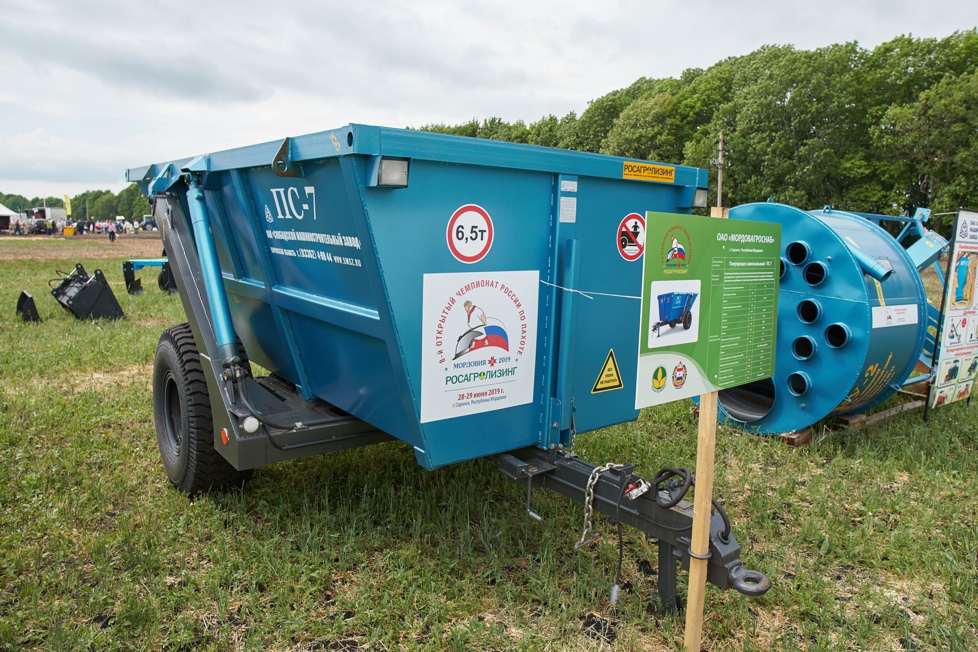 A bright blue farm trailer with a load capacity sign, parked in a grassy field on a cloudy day.