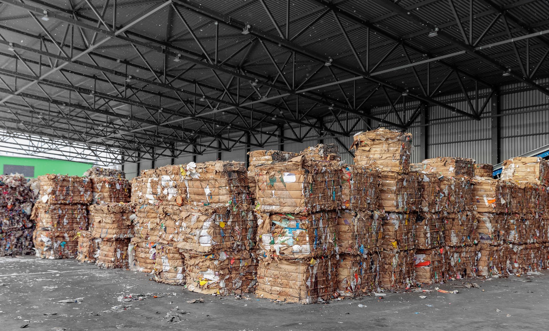 Large, neatly stacked rectangular bales of compressed cardboard and paper waste stored in a spacious warehouse.