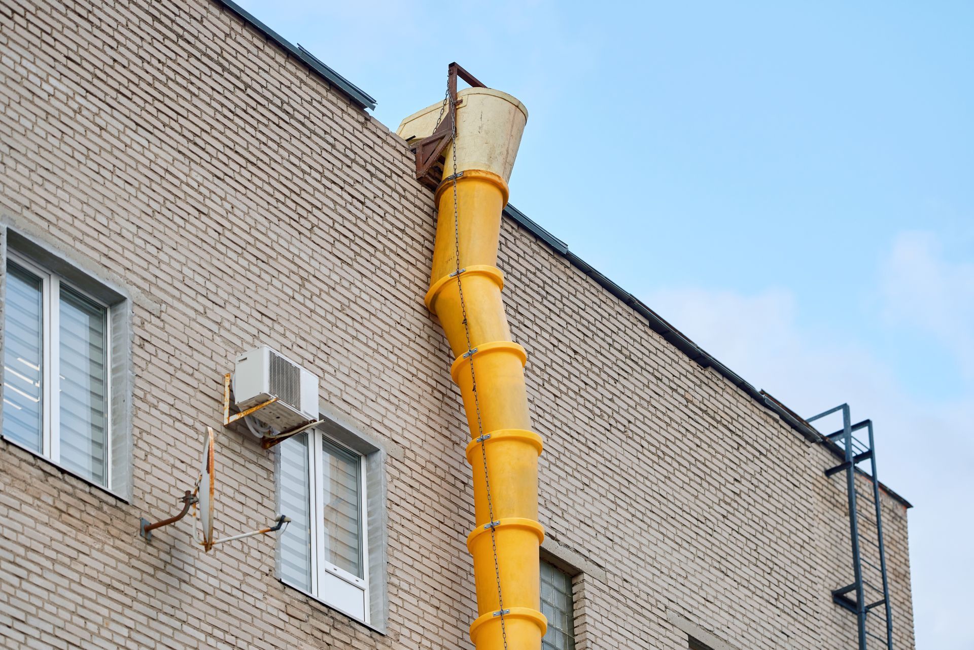 A yellow plastic construction debris chute attached to the roof of a brick building.