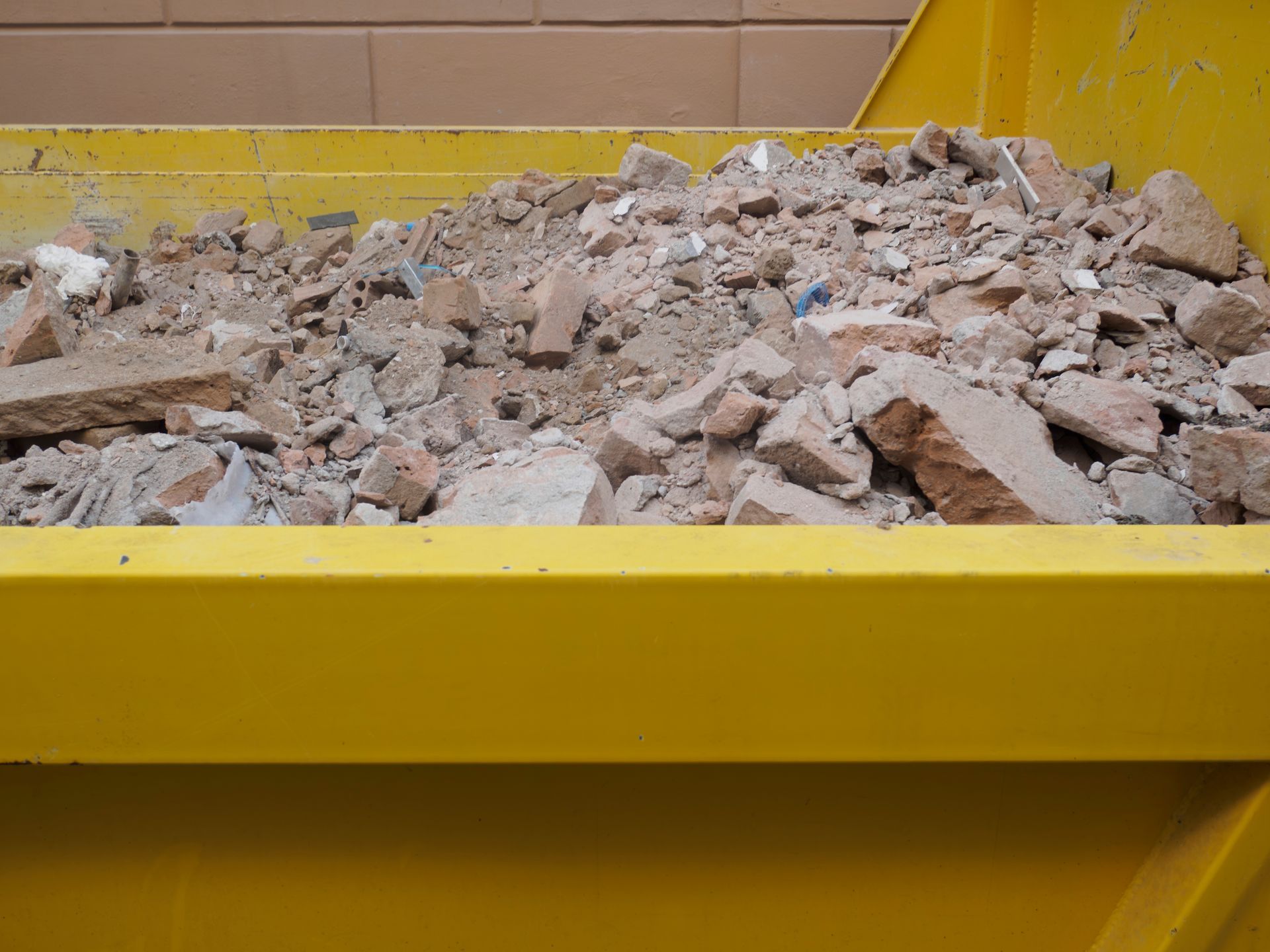 A bright yellow dumpster filled with rubble, broken bricks, and concrete debris.