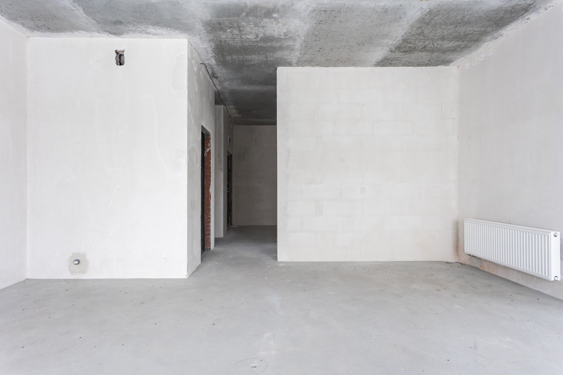 An unfinished interior room with white walls, a gray concrete floor, an exposed concrete ceiling, and a white radiator.
