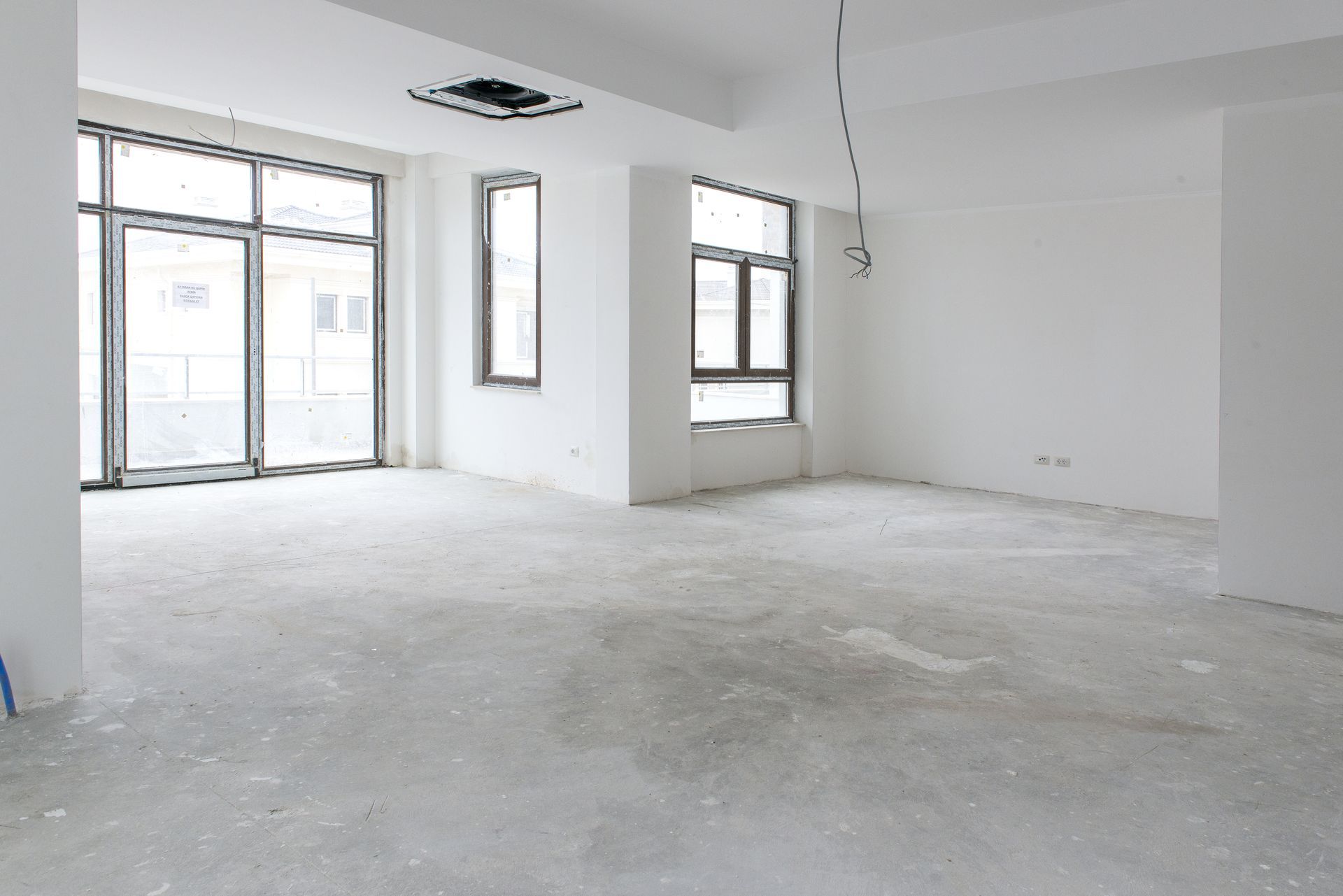 An empty, unfinished room with white walls, a concrete floor, and large glass windows and doors.