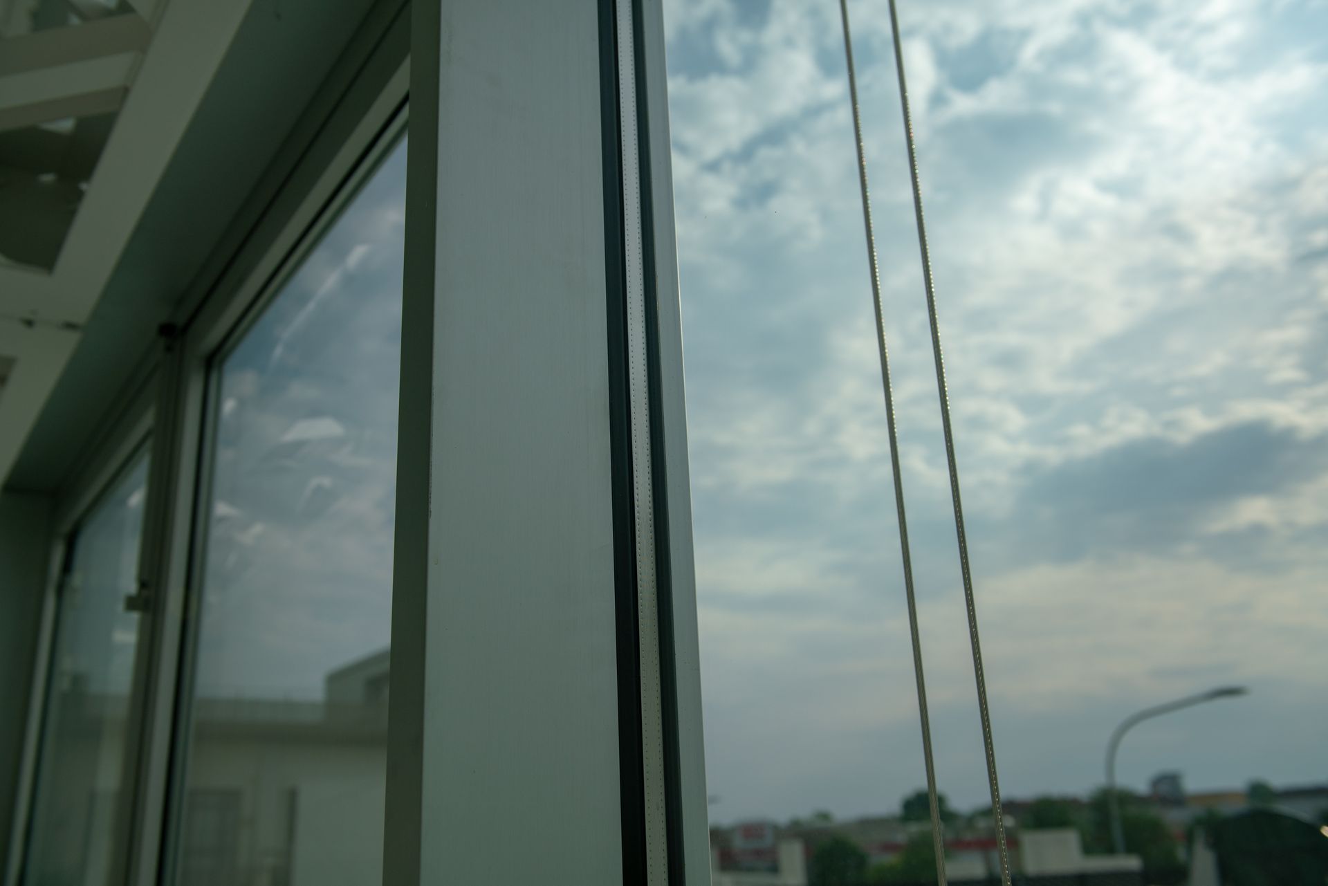 A close-up view of a white window frame with a black sealant strip against a cloudy sky and distant buildings.