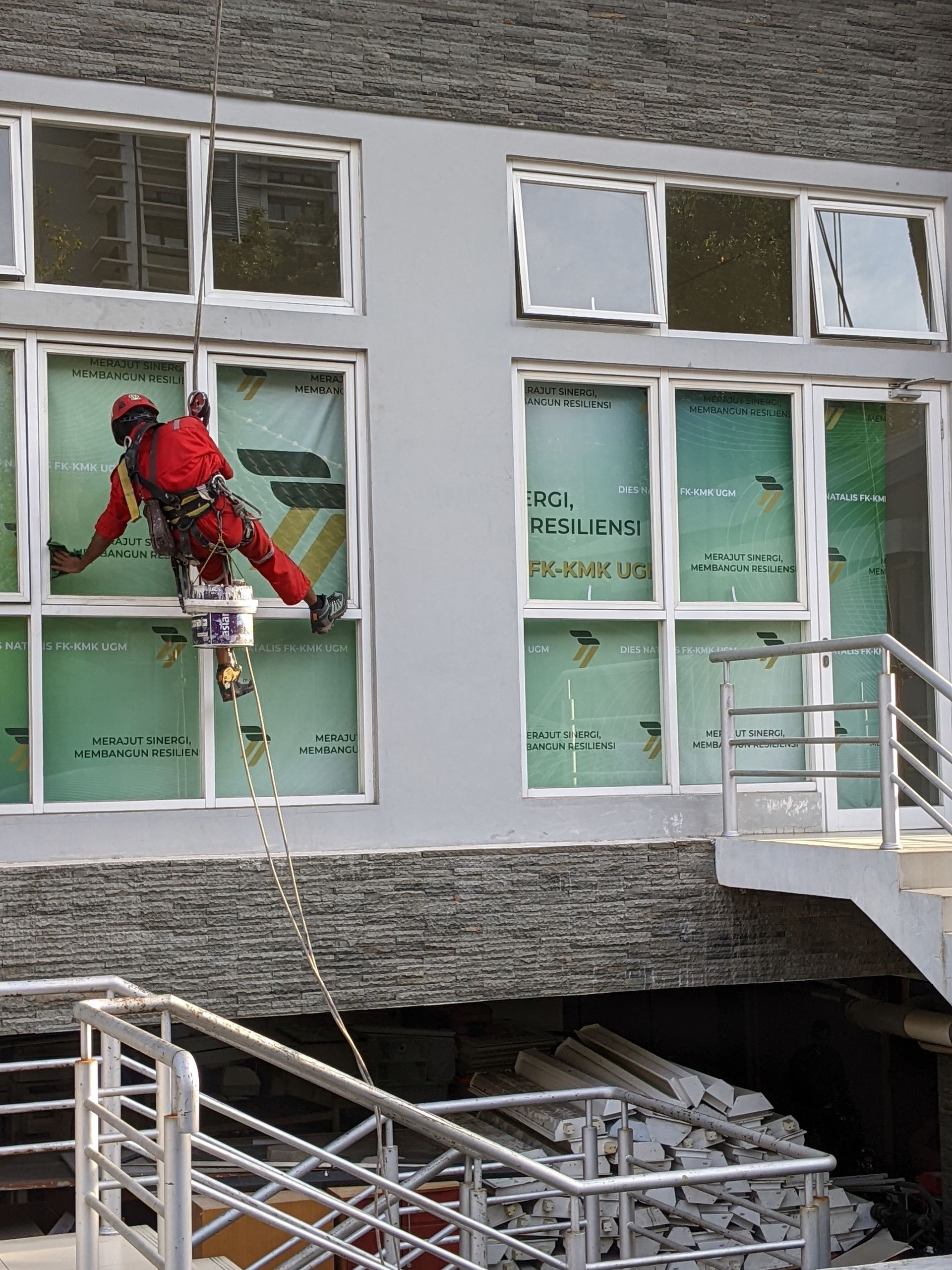 A person in a red uniform and safety harness rappels down the side of a building, cleaning windows.