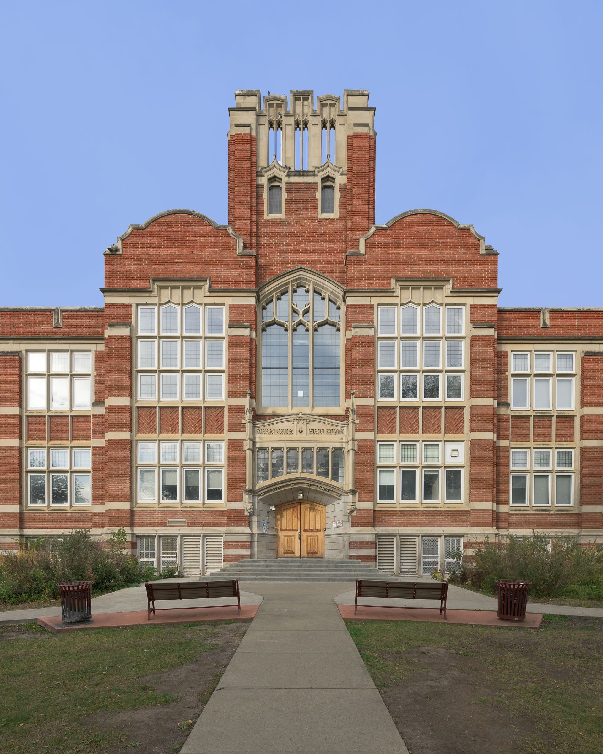 Front view of a red-brick school building with arched central entrance and a walkway leading to it