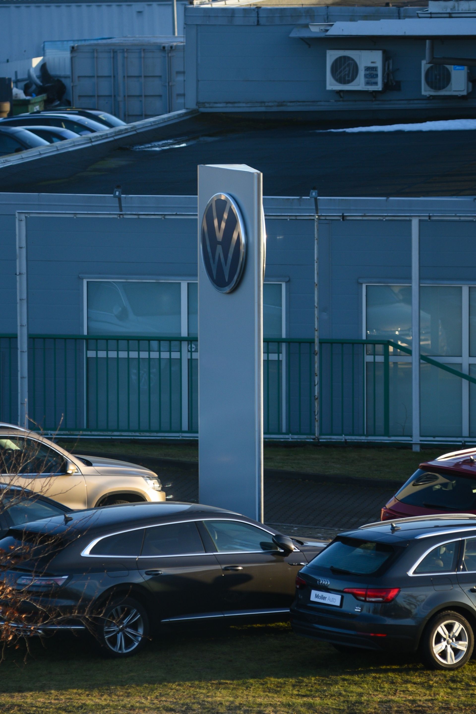 Volkswagen dealership lot with parked cars in front of a blue building and VW logo sign