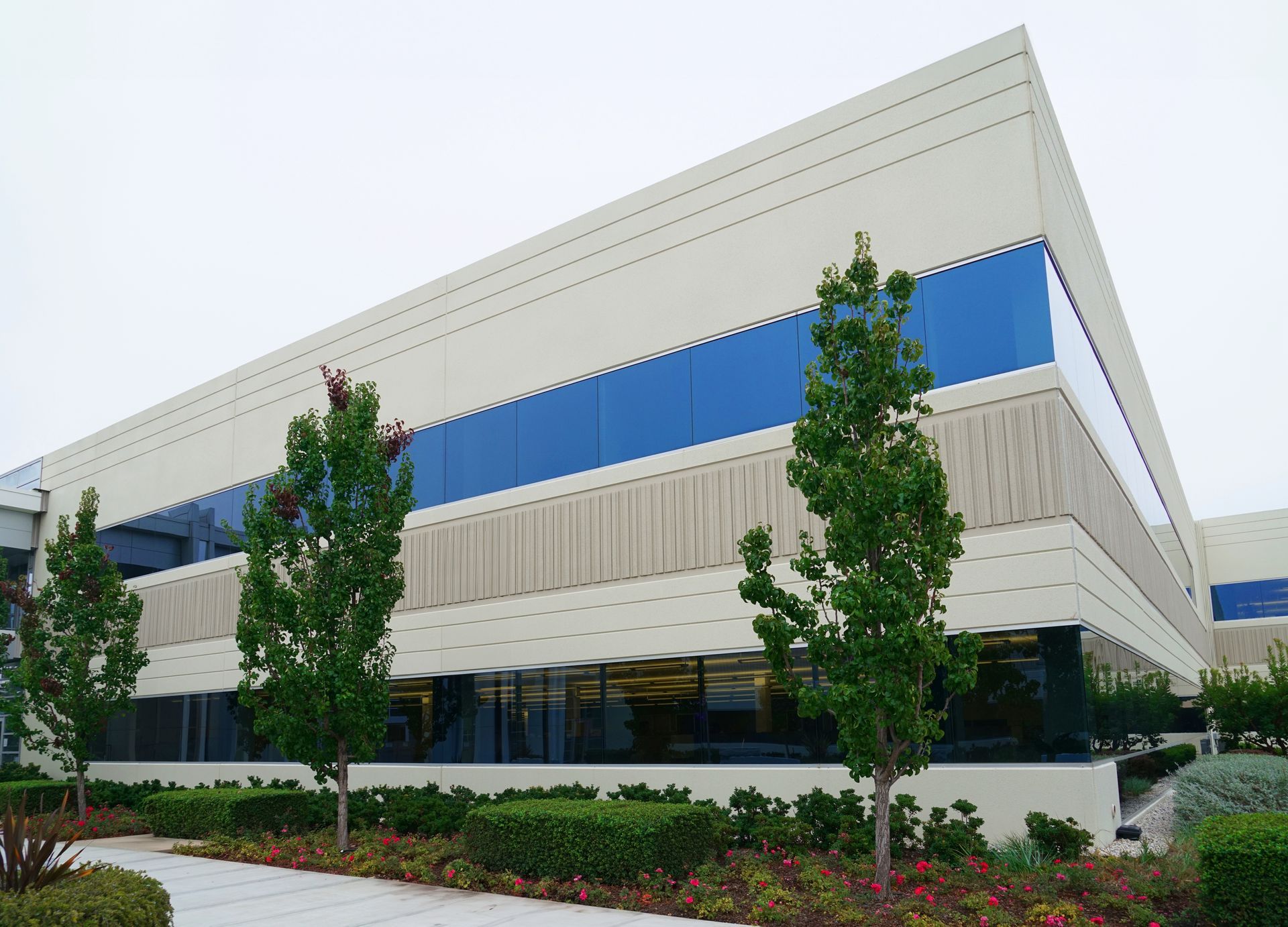 A modern two-story commercial building with light beige walls and horizontal blue window bands, set behind landscaping.