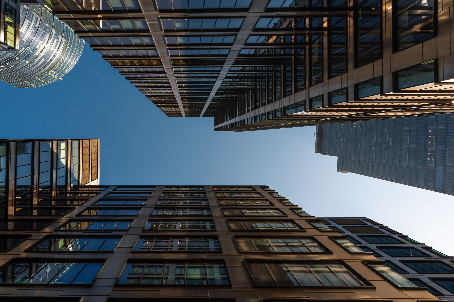 Low-angle view of multiple modern glass and steel skyscrapers reaching into a clear blue sky in a city.