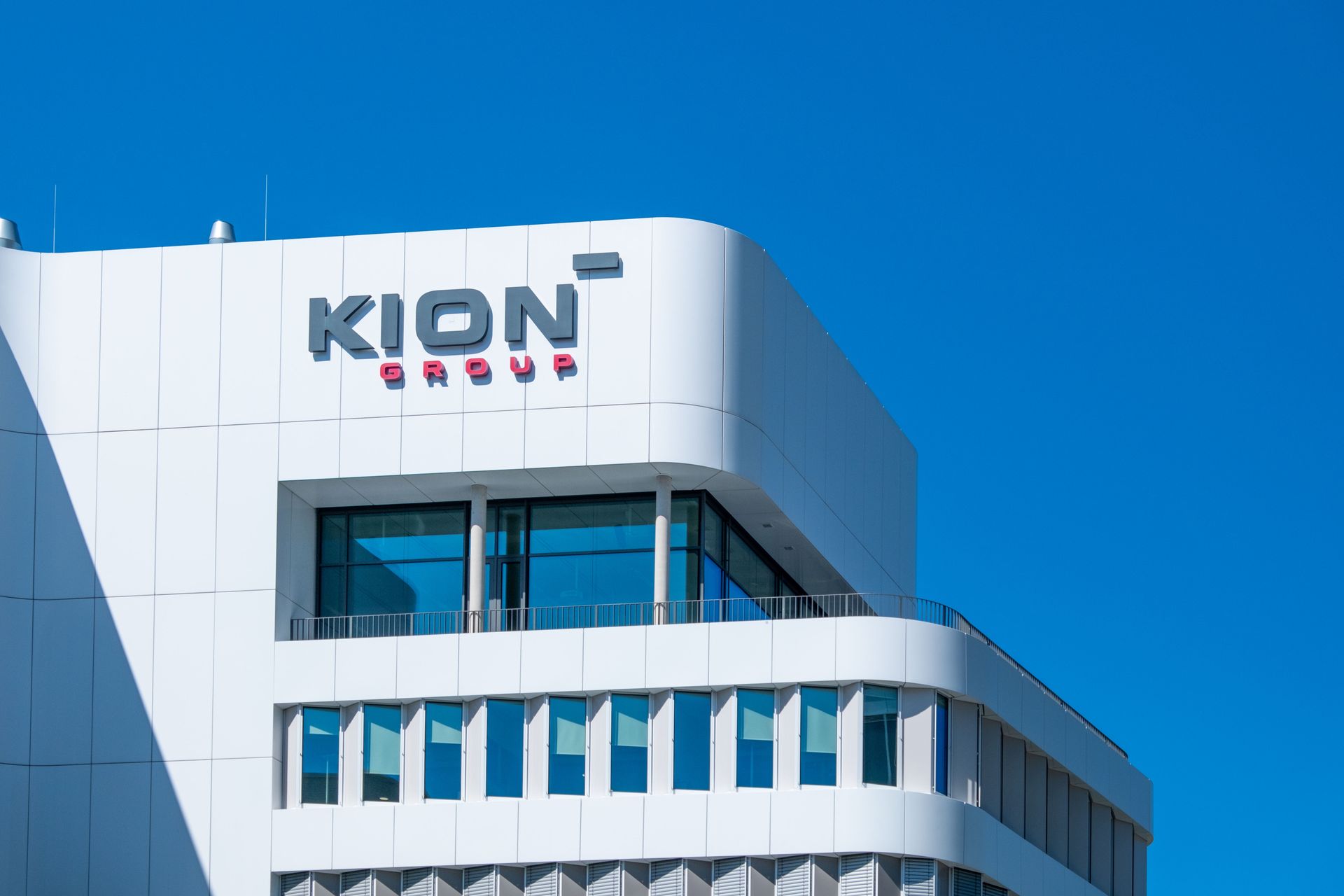 A low-angle view of the white exterior of the KION Group headquarters building under a clear blue sky.
