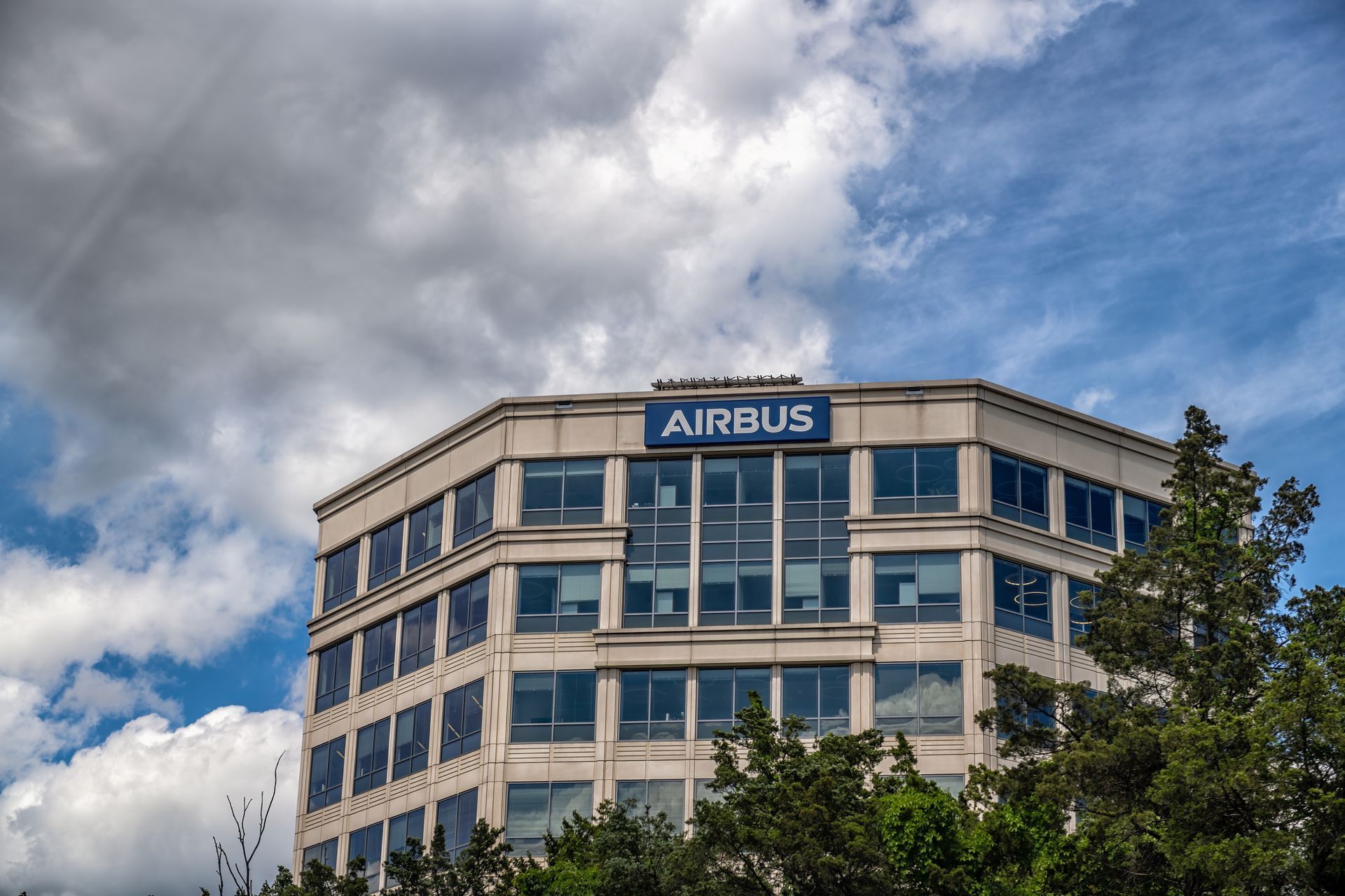 The Airbus corporate headquarters building, a multi-story office block with glass windows, set against a cloudy blue sky.