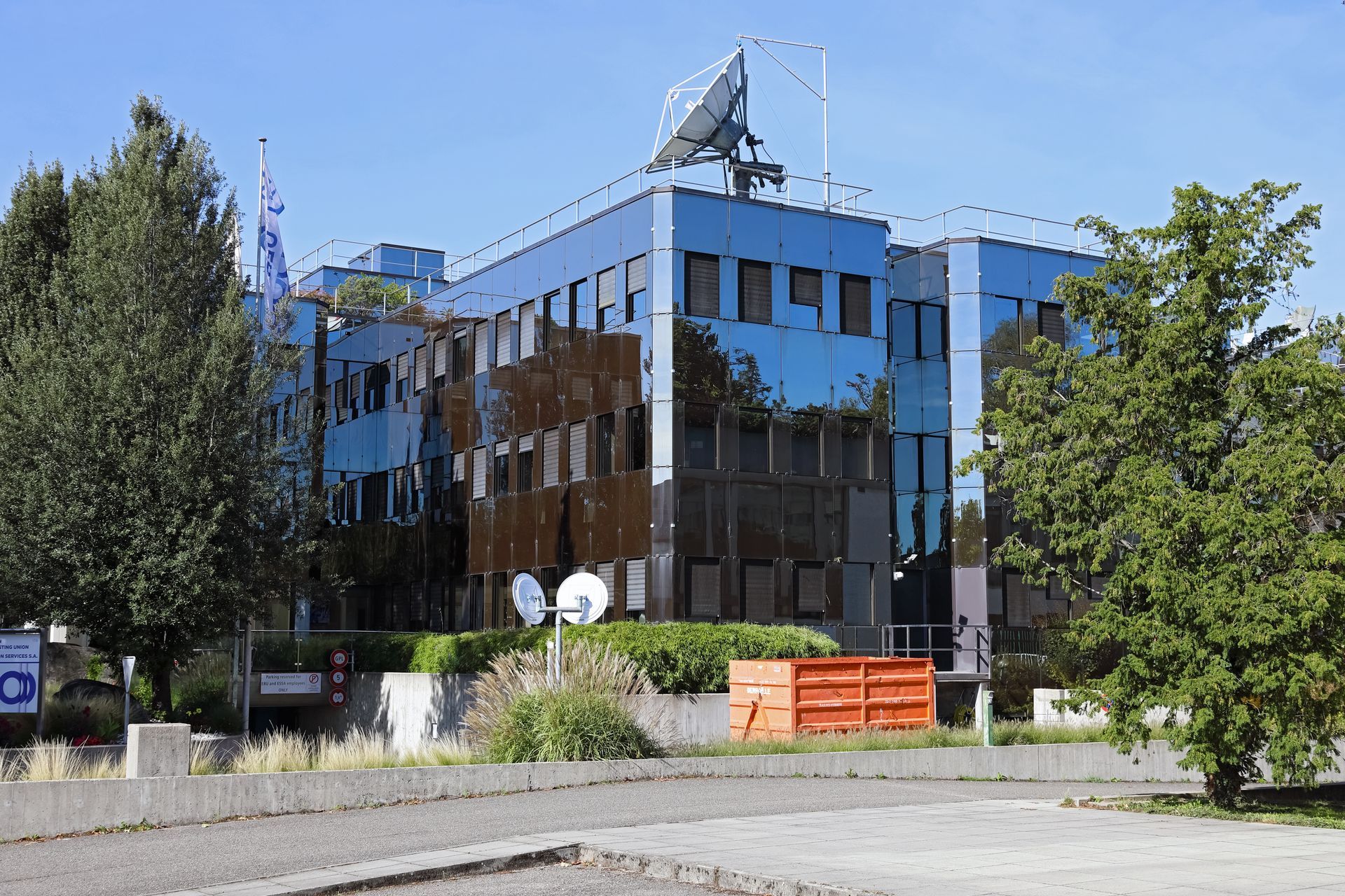 A multi-story office building with a reflective, blue-tinted glass facade and a rooftop satellite dish.