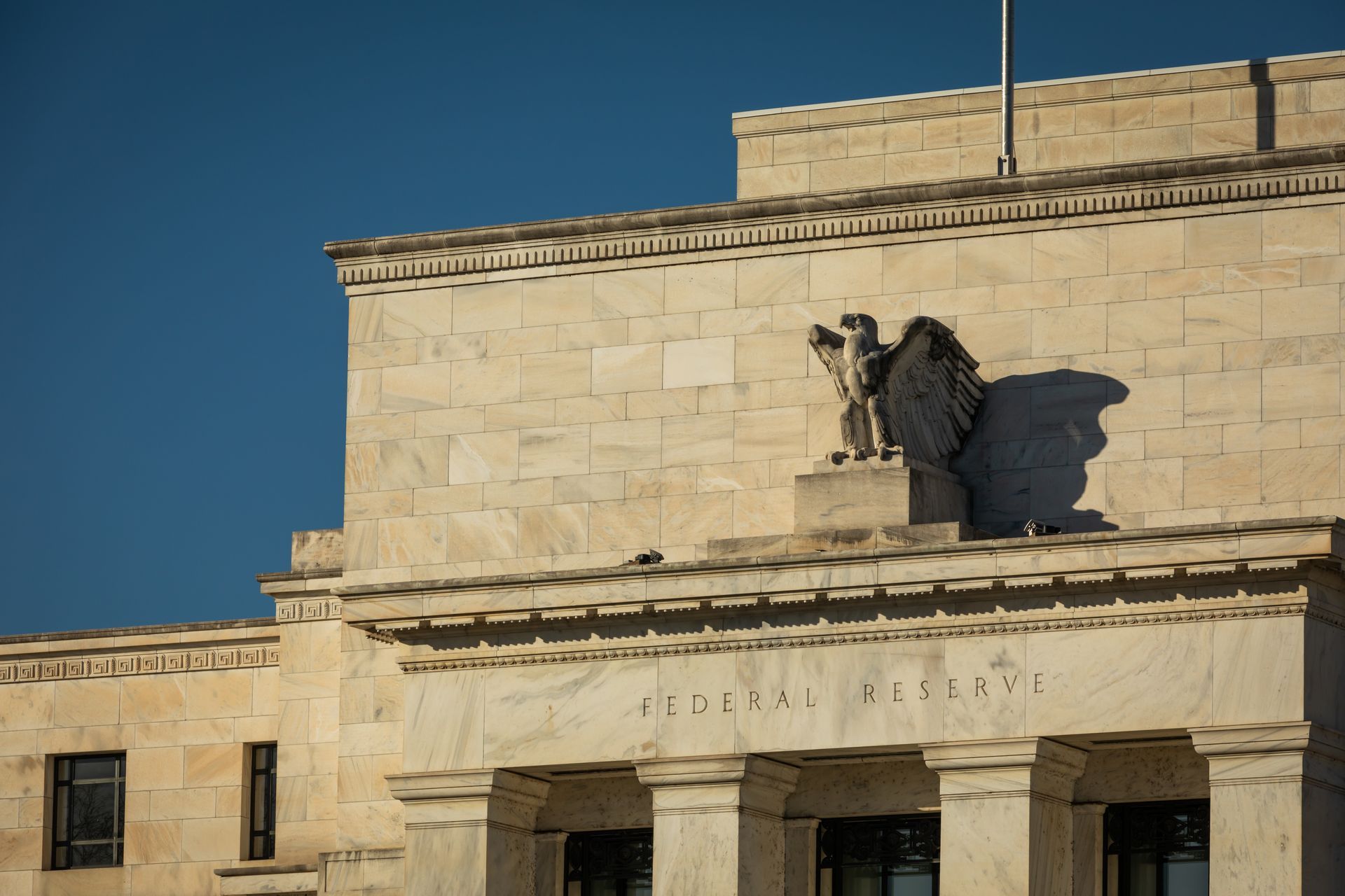 The stone facade of the Federal Reserve building with its eagle sculpture, under a clear blue sky.