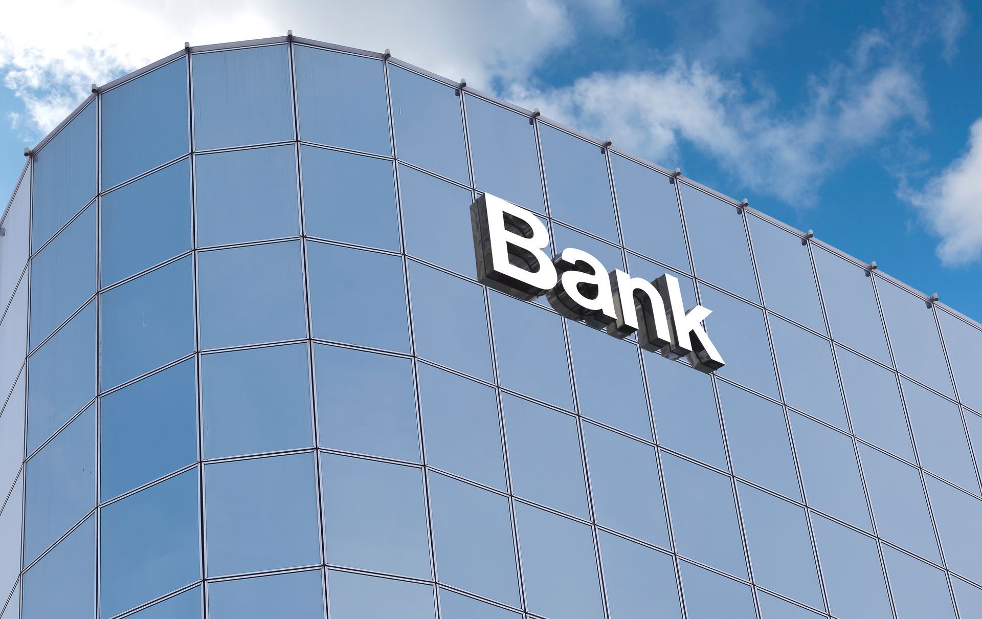 A modern bank building with a reflective glass exterior facade against a blue sky with white clouds.