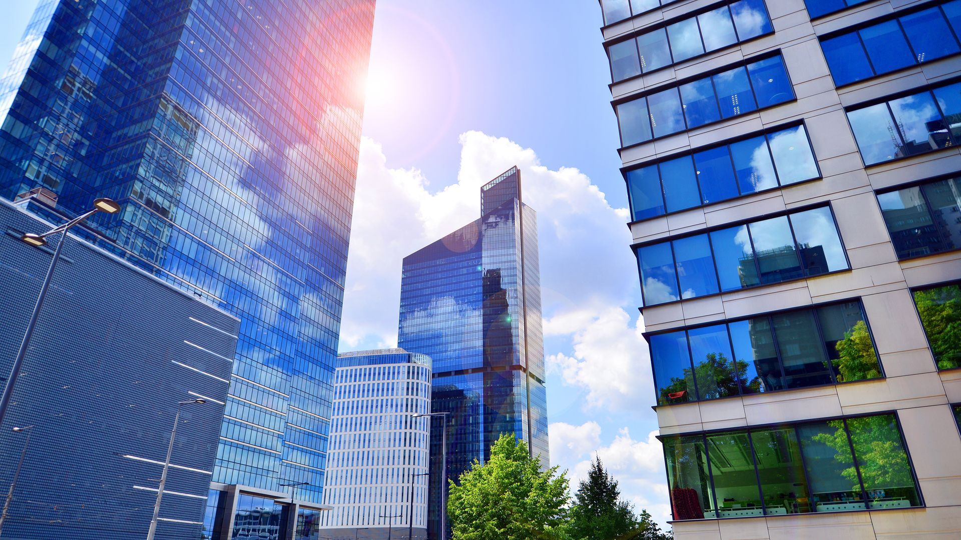 Modern office skyscrapers with glass facades reflecting the blue sky and clouds under bright sunlight.