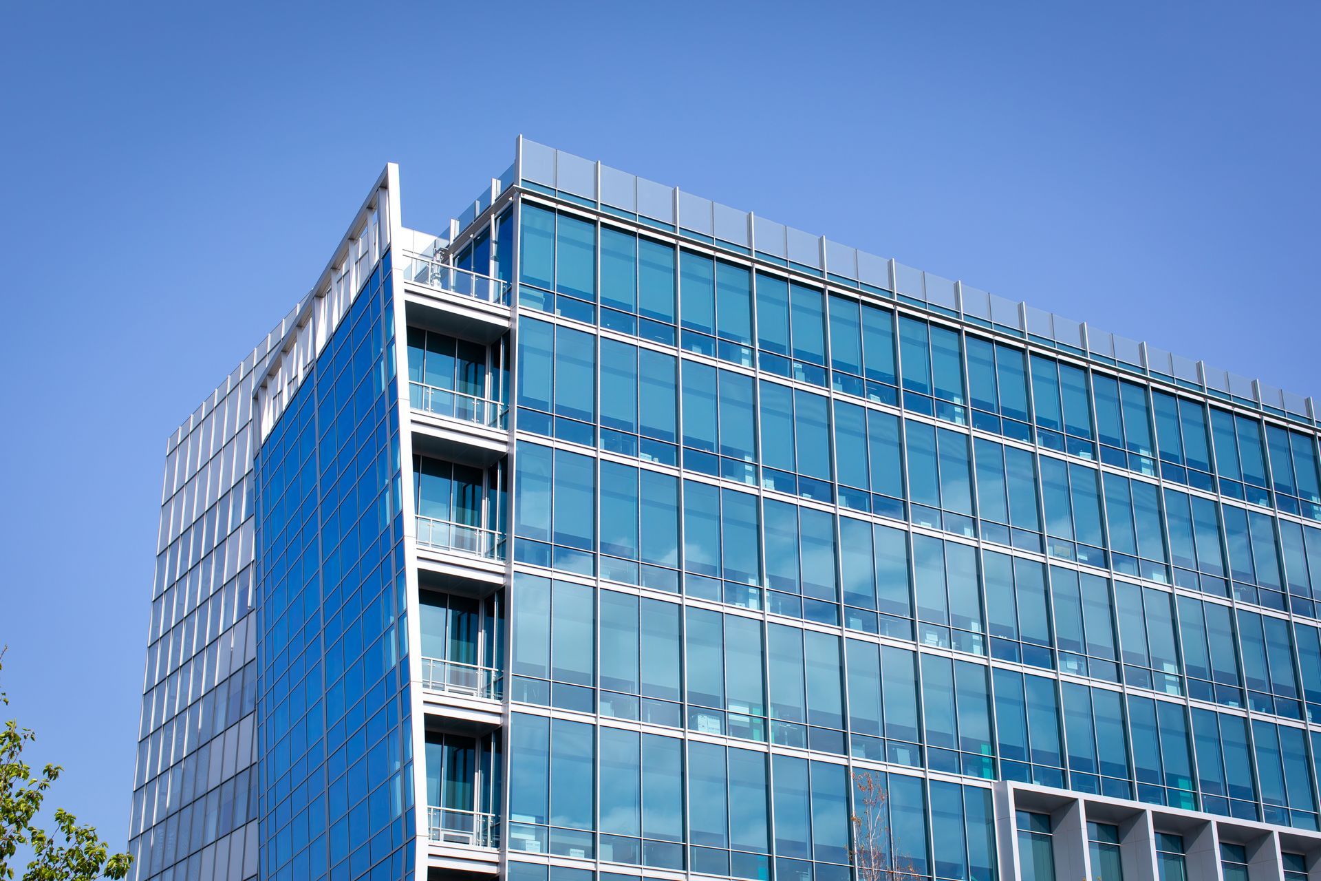A modern building with a blue glass facade, a blue textured side wall, and visible balconies against a clear blue sky.