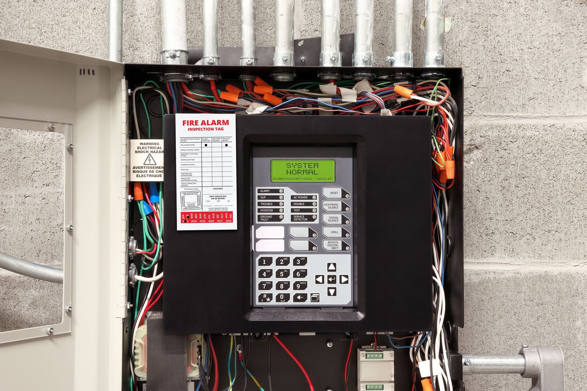 A fire alarm control panel with an open cabinet, showing internal wiring, mounted on a grey cinder block wall.