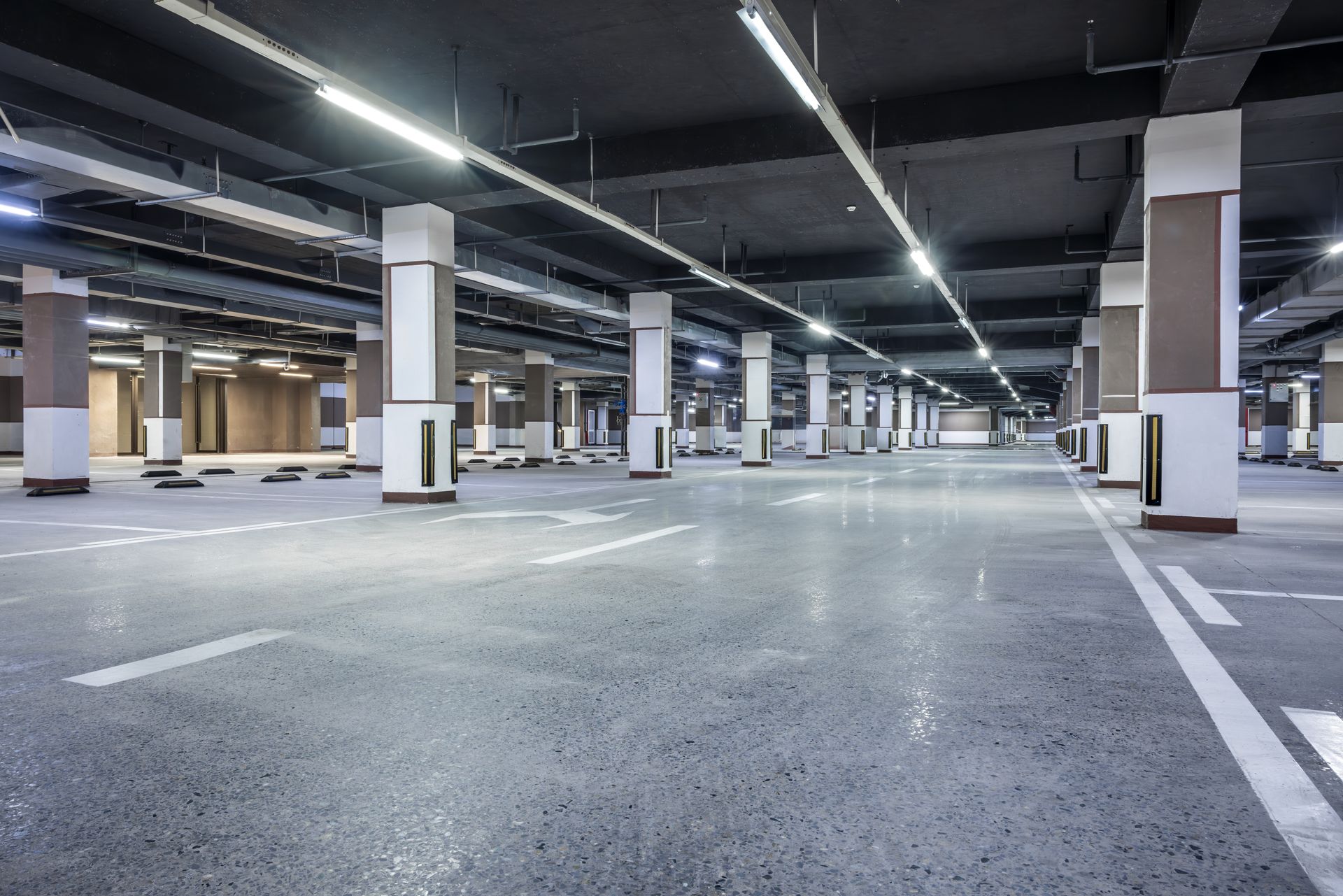 An empty, brightly lit underground parking garage with concrete floors and support pillars.