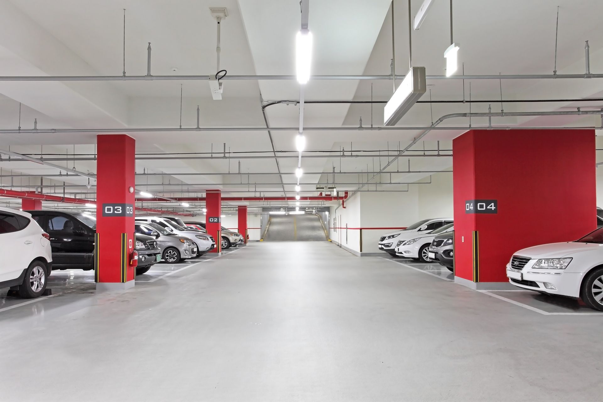 Underground parking garage with parked cars, marked by red pillars and fluorescent lighting.