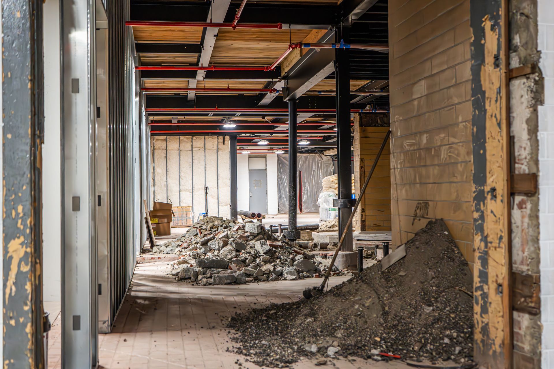 An interior view of a building under construction, featuring exposed steel beams, rubble, and piles of dirt on the floor.