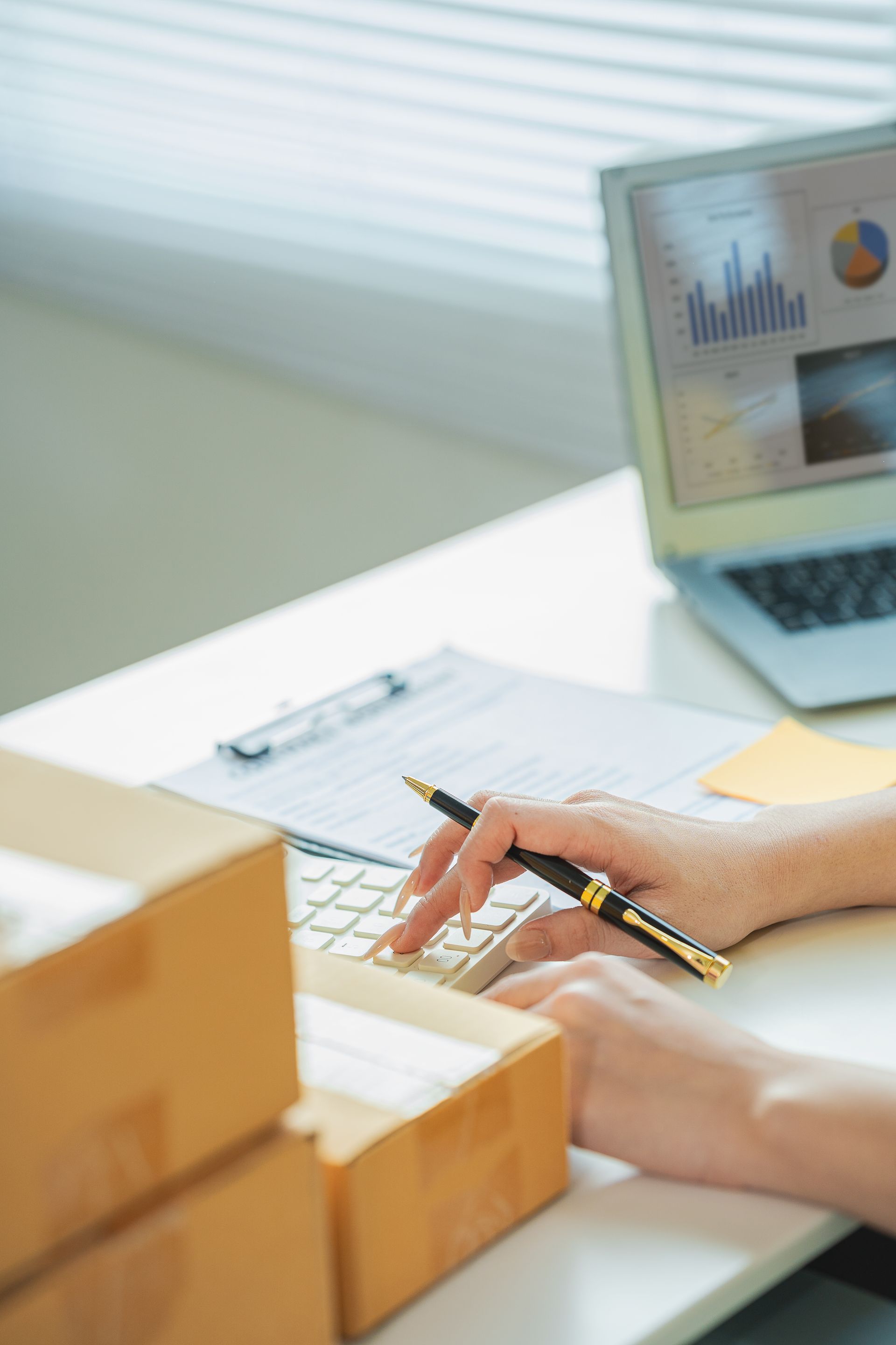 Hands writing on a keyboard beside a laptop displaying charts in a bright office