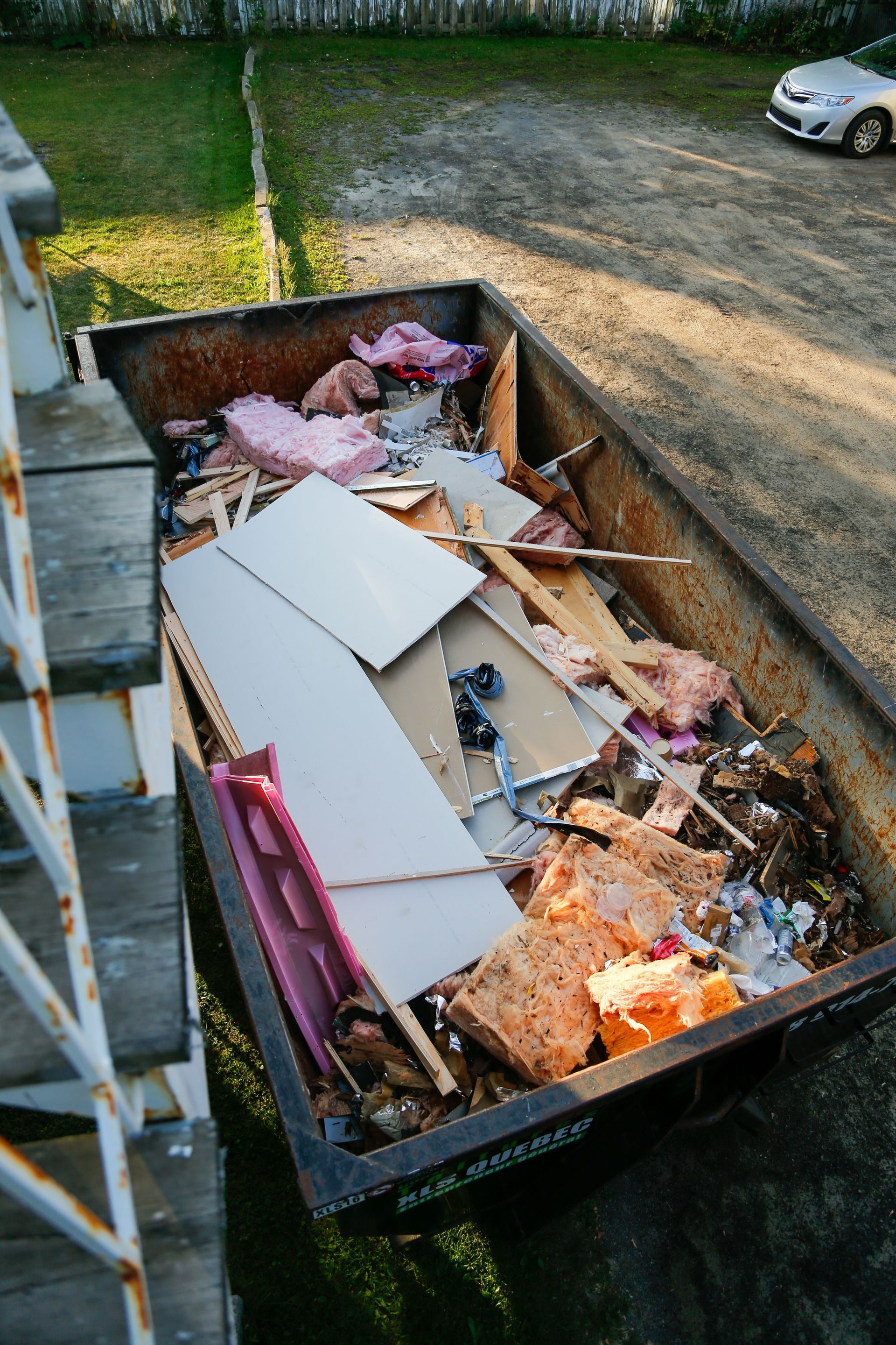 Dumpster filled with construction debris and pink insulation in a gravel lot