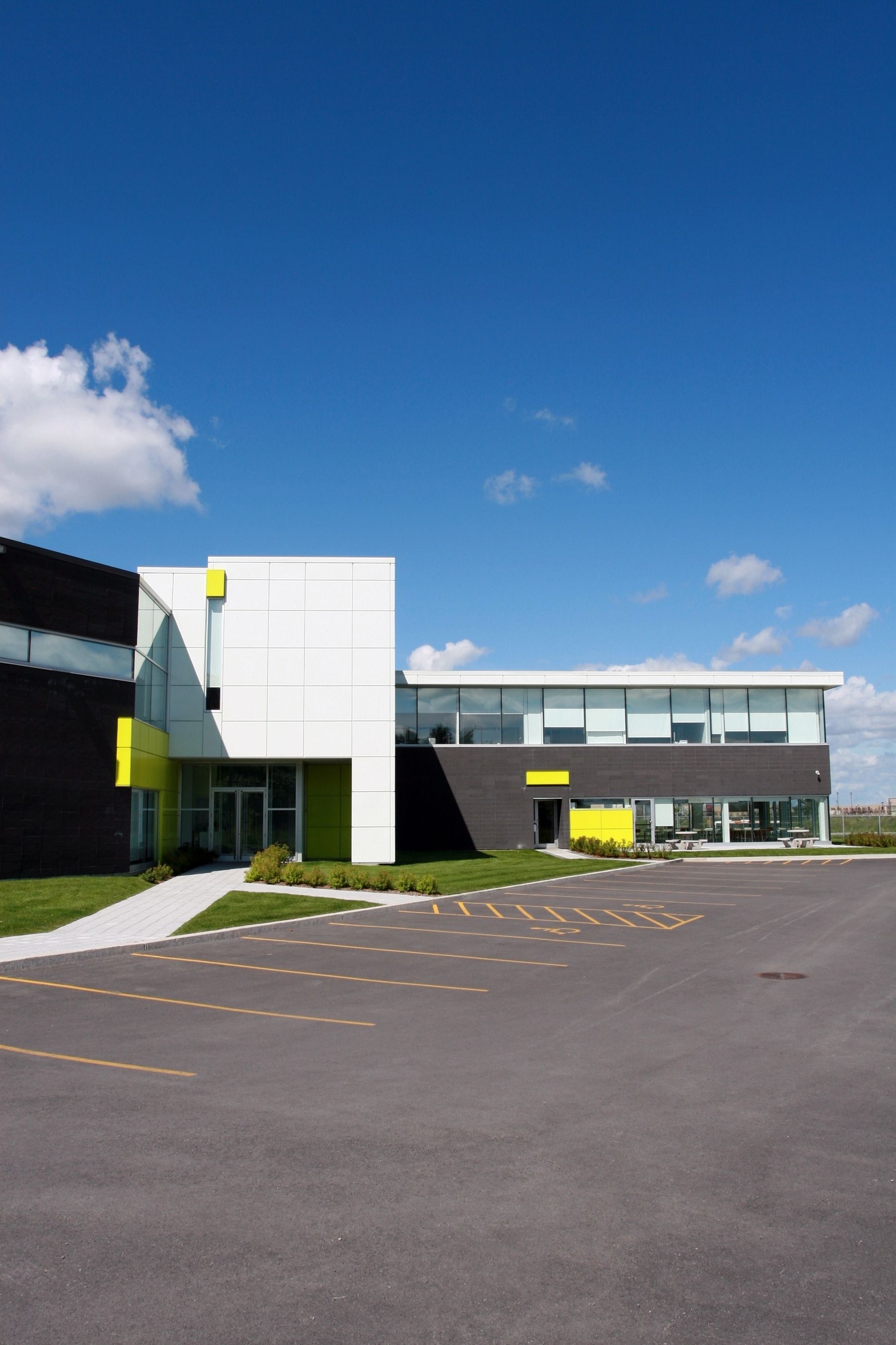 Modern building with white and gray panels beside an empty parking lot under a clear blue sky