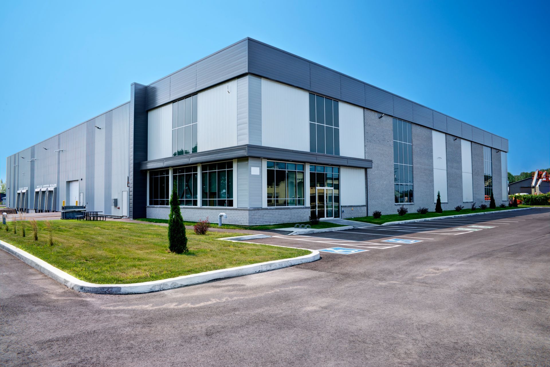 A modern, single-story gray commercial or industrial building with large windows and a paved parking lot on a sunny day.