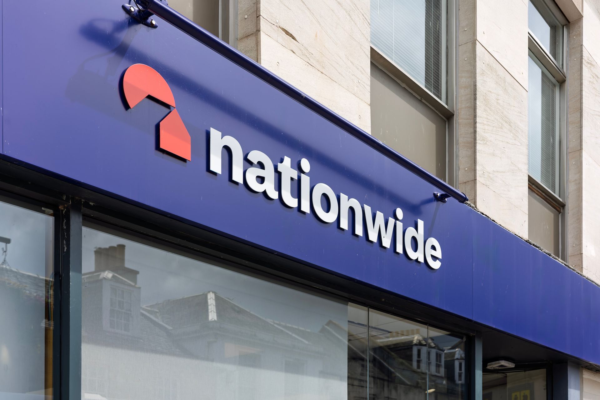 A close-up view of the Nationwide building society logo and name on a dark blue storefront sign above a window.