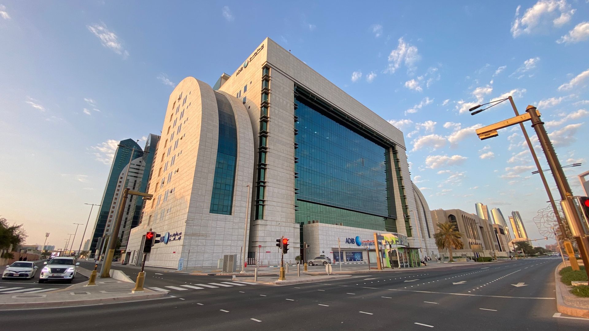 A modern, white stone and glass office building under a blue sky, viewed from a street intersection at sunset.