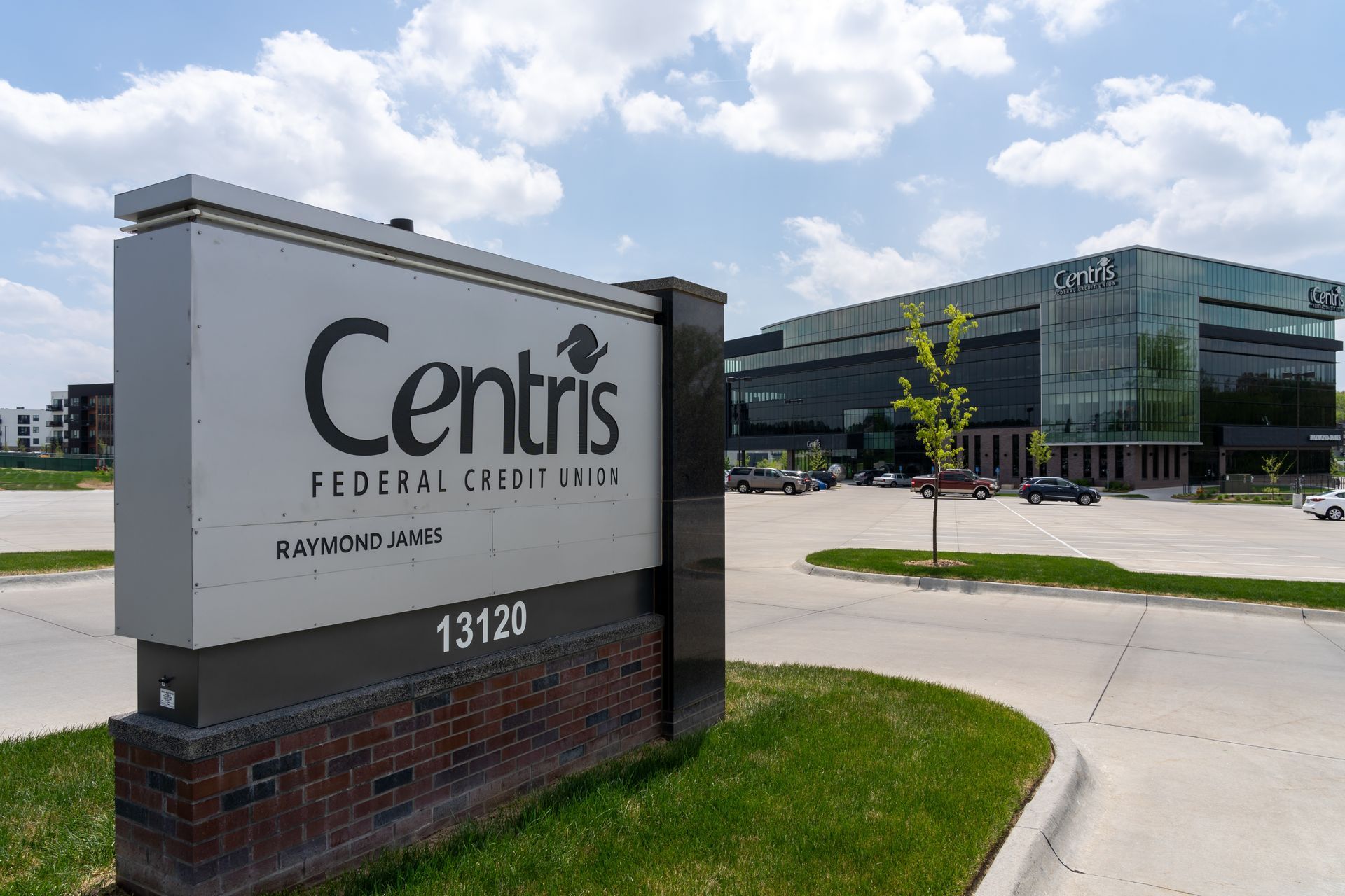 A gray sign for Centris Federal Credit Union at 13120 stands in front of a modern glass office building under a blue sky.
