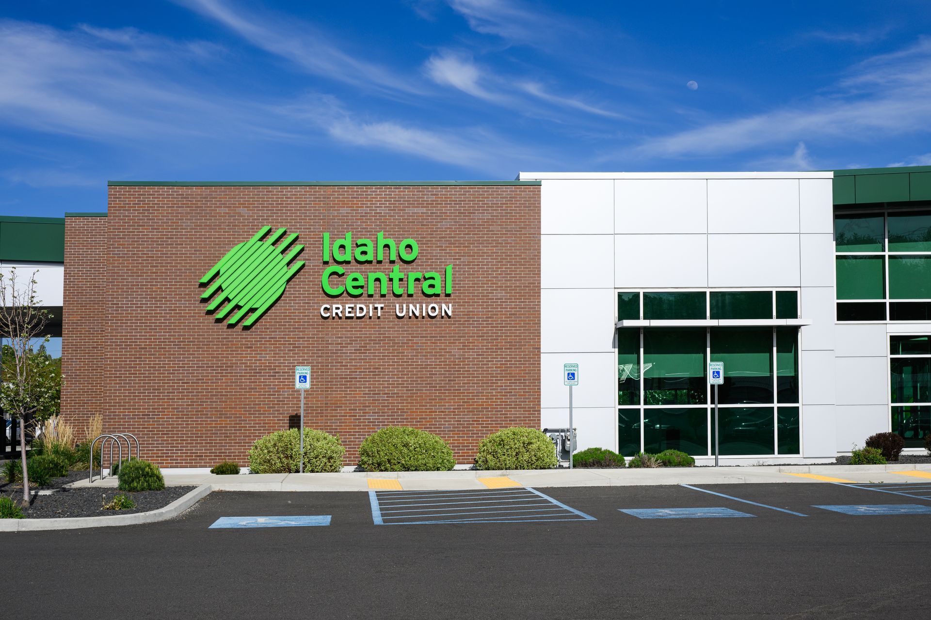 Exterior view of an Idaho Central Credit Union branch with brick and white panels, green logo, and parking lot in front.