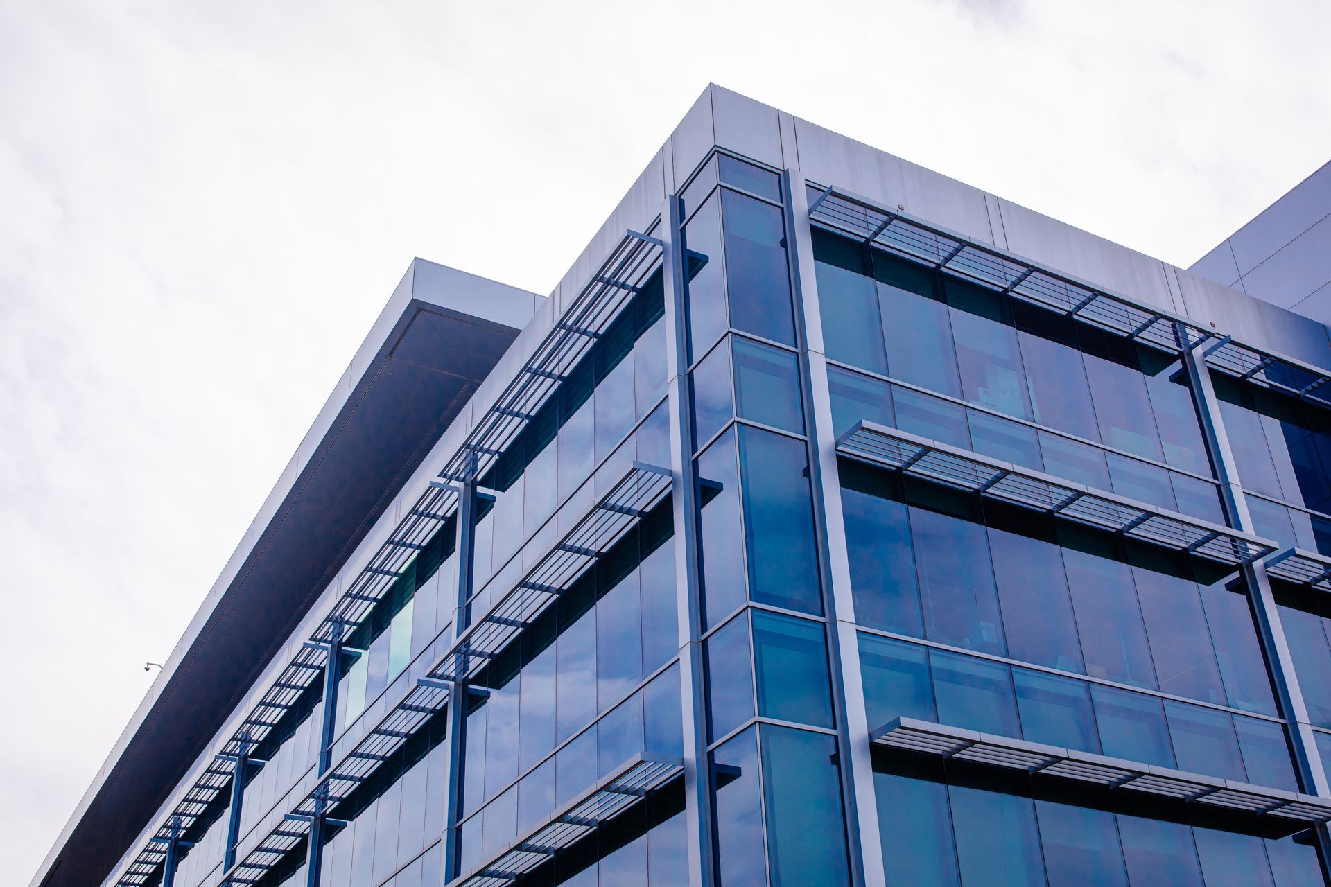 A low-angle view of a modern office building with a glass facade, reflective windows, and metallic architectural details.