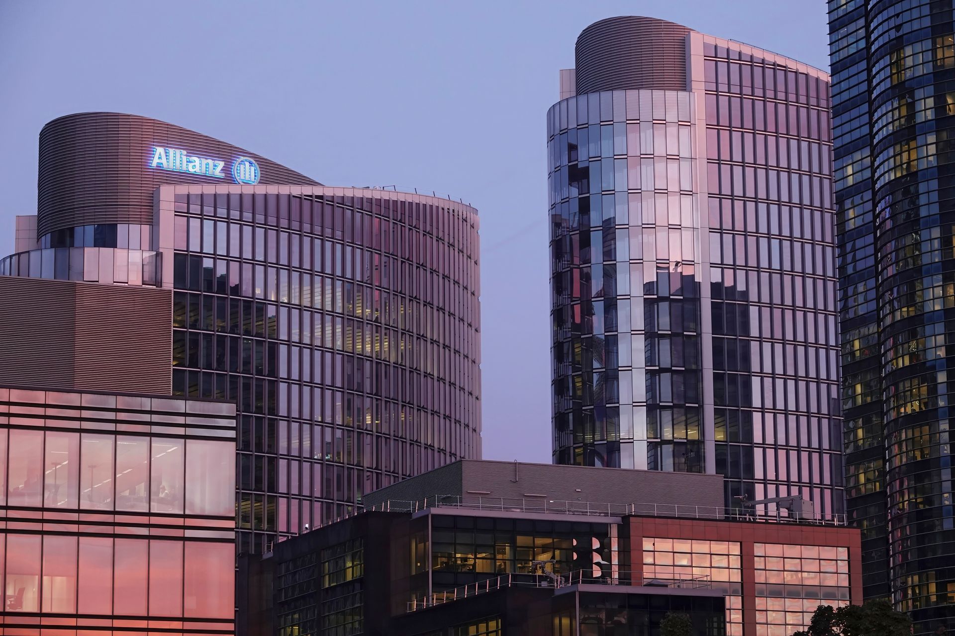Modern office buildings with glass facades reflect a soft sunset glow under a clear evening sky.