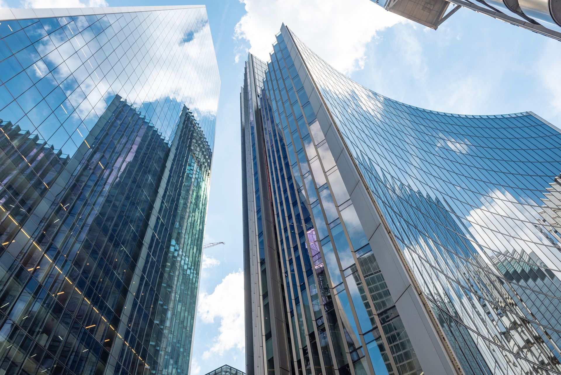 Low-angle view of modern glass skyscrapers reaching toward a blue, partly cloudy sky.