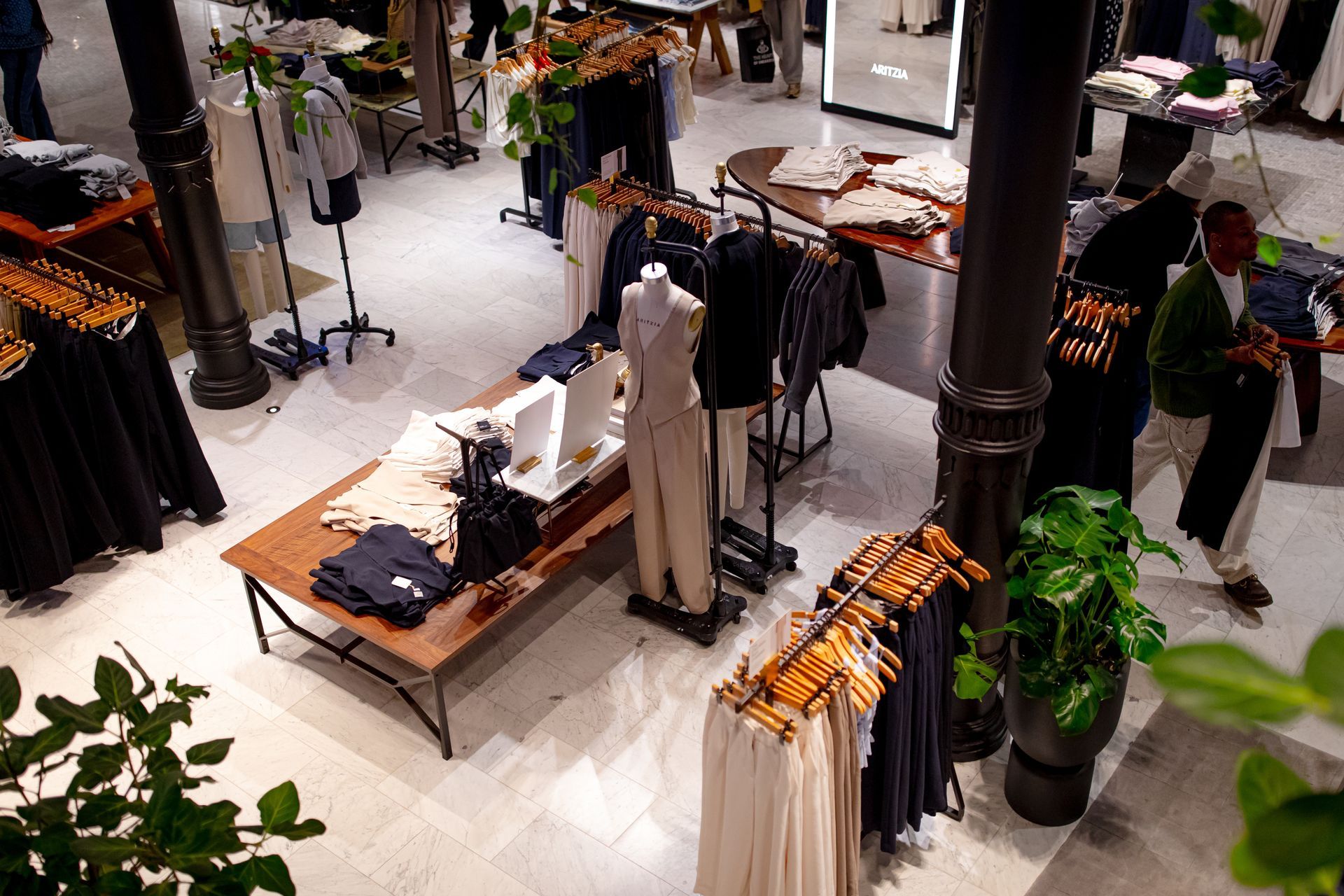 An elevated view of a retail clothing store with tables, racks of garments, and a person walking through the aisles.